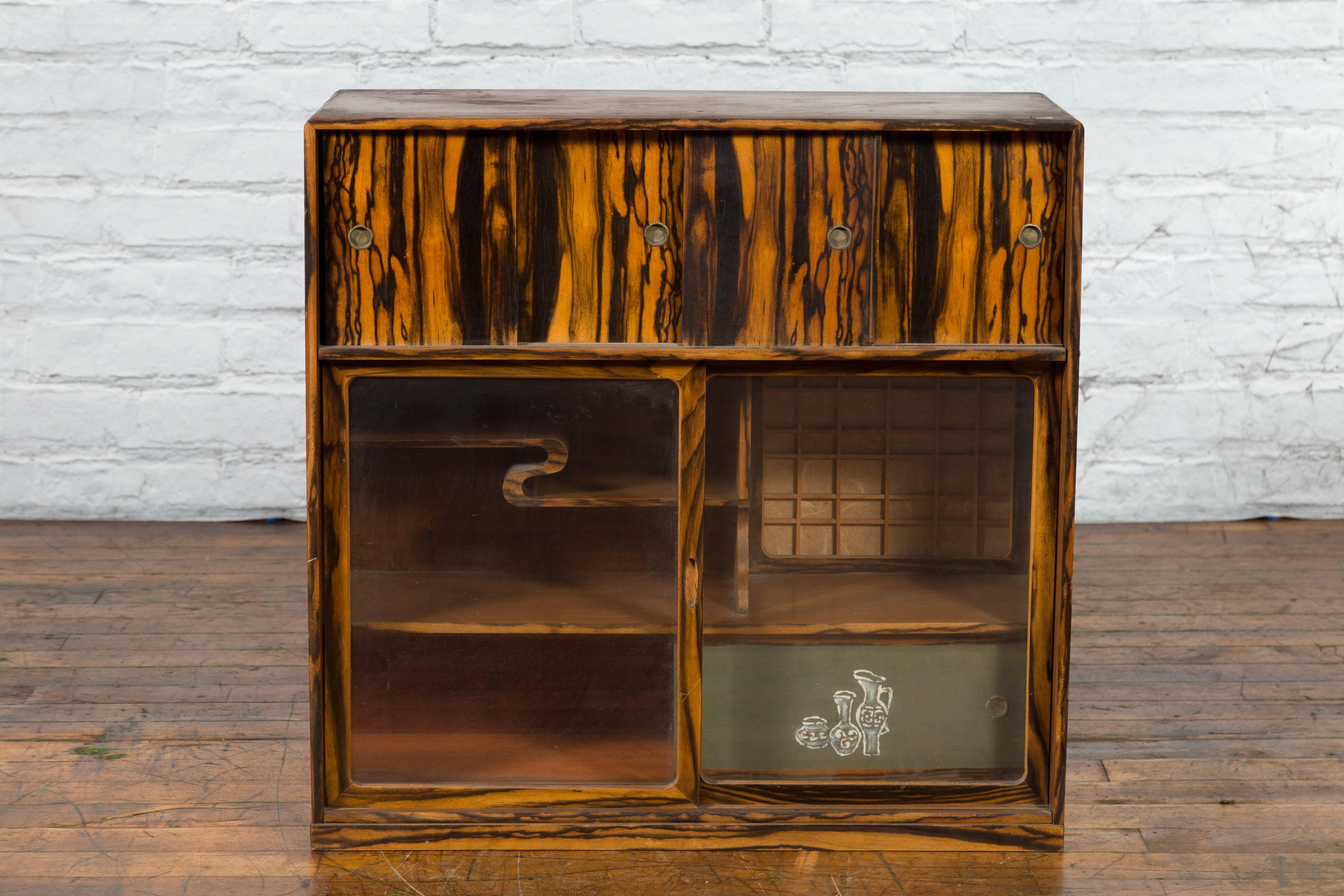 A Japanese zebra wood tansu chest from the 19th century, with sliding doors, glass panels and secret storage. Created in Japan during the 19th century, this tansu chest features a linear silhouette perfectly complimented by its zebra wood grain. A
