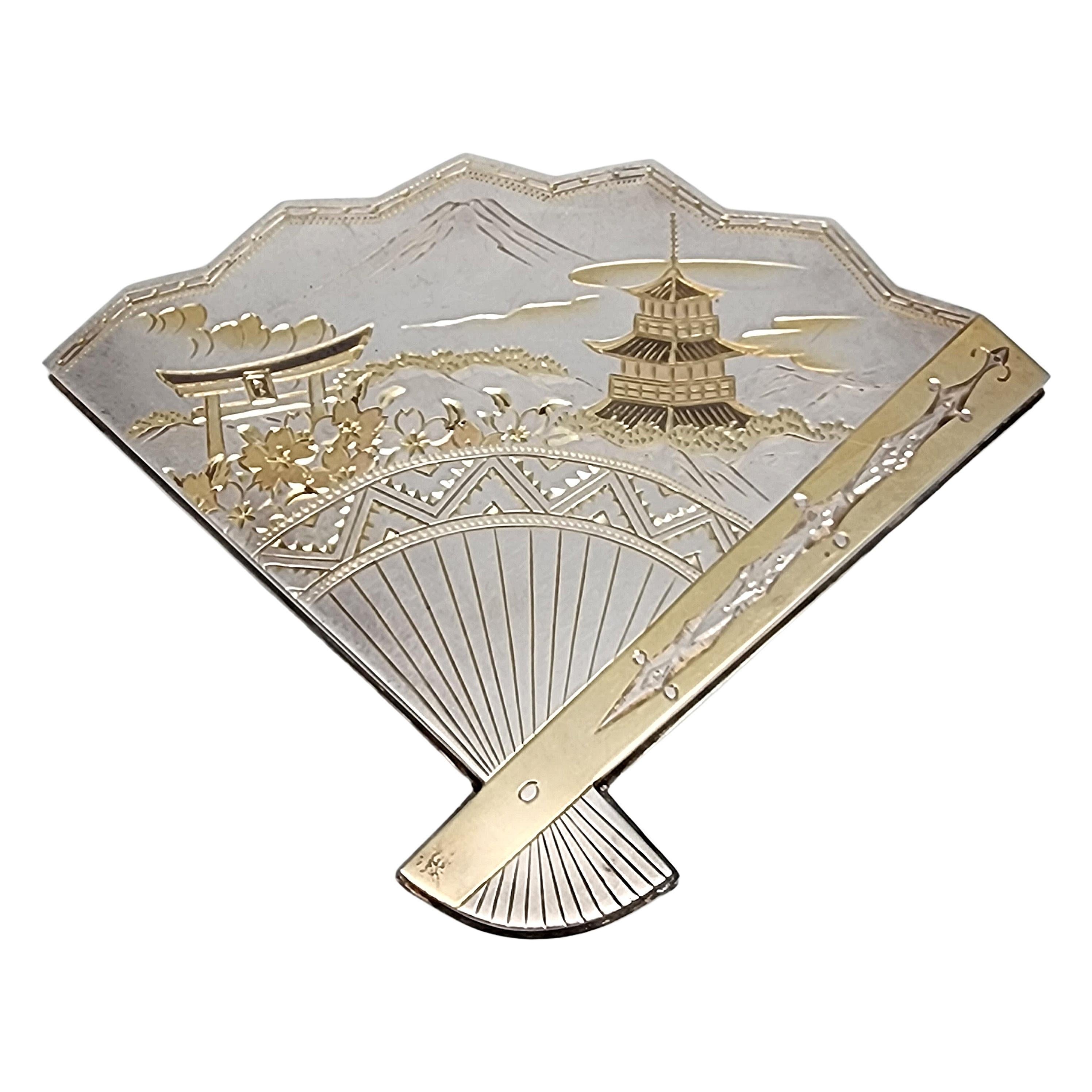 Vintage sterling silver with yellow gold accent fan mirror compact with box.

Beautiful fan shape with etched designs featuring a mountain, pagoda, Torii gate and flower scene with yellow gold accents. The back features a smooth polished design with