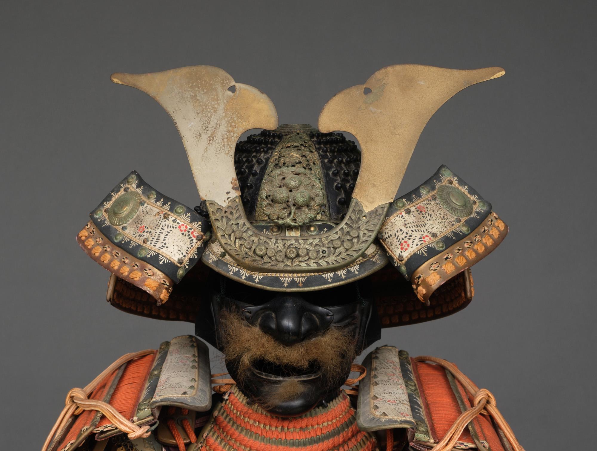 Ein auffälliger japanischer Goldlack-ô'yoroi (große Rüstung) mit leuchtend orangefarbenen Corden, einem mehrfarbigen und hellorangen Saum (kin'urushinuri hi'ito hi'suso tôsei gusoku ô'yoroi).

- 28-teiliger schwarzer Lack-Koboshi'bachi kabuto (Helm