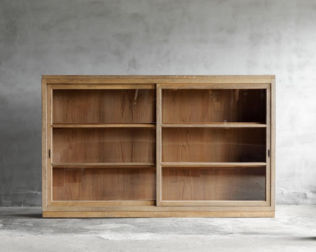This elegant, slim cabinet is a unique piece from the olden days of the Showa era.
Its transparent glass doors beautifully showcase the contents inside. 
The cabinet is crafted from high-quality oak wood, featuring a naturally aged, muted color that