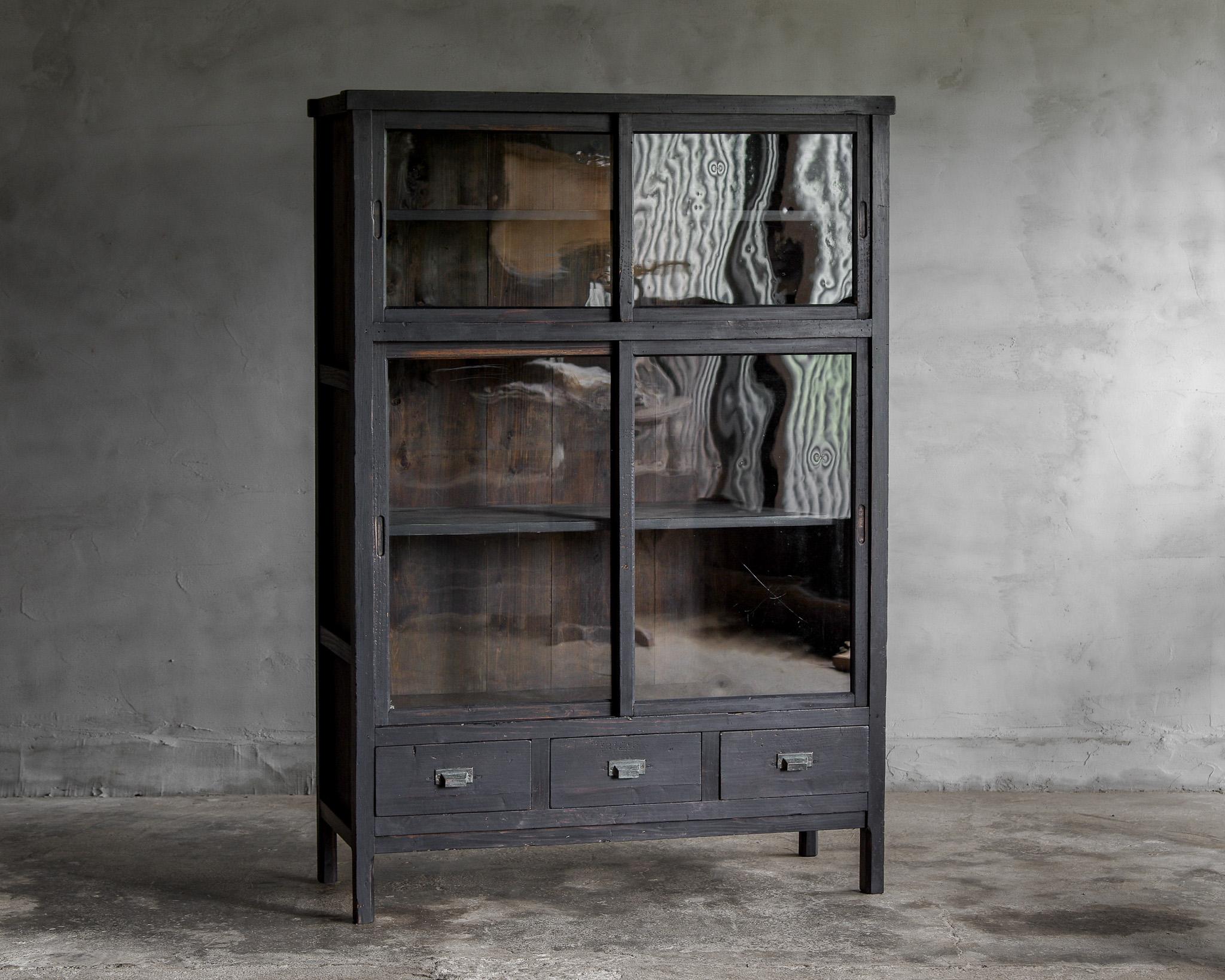 This is a very old cabinet from the Late Meiji -Taisho Period (Early 1900s). 

It is very old. The matte black color is very stylish. The glass is original from that time, which gives it a beautiful shimmer. 
It is a wonderful design that