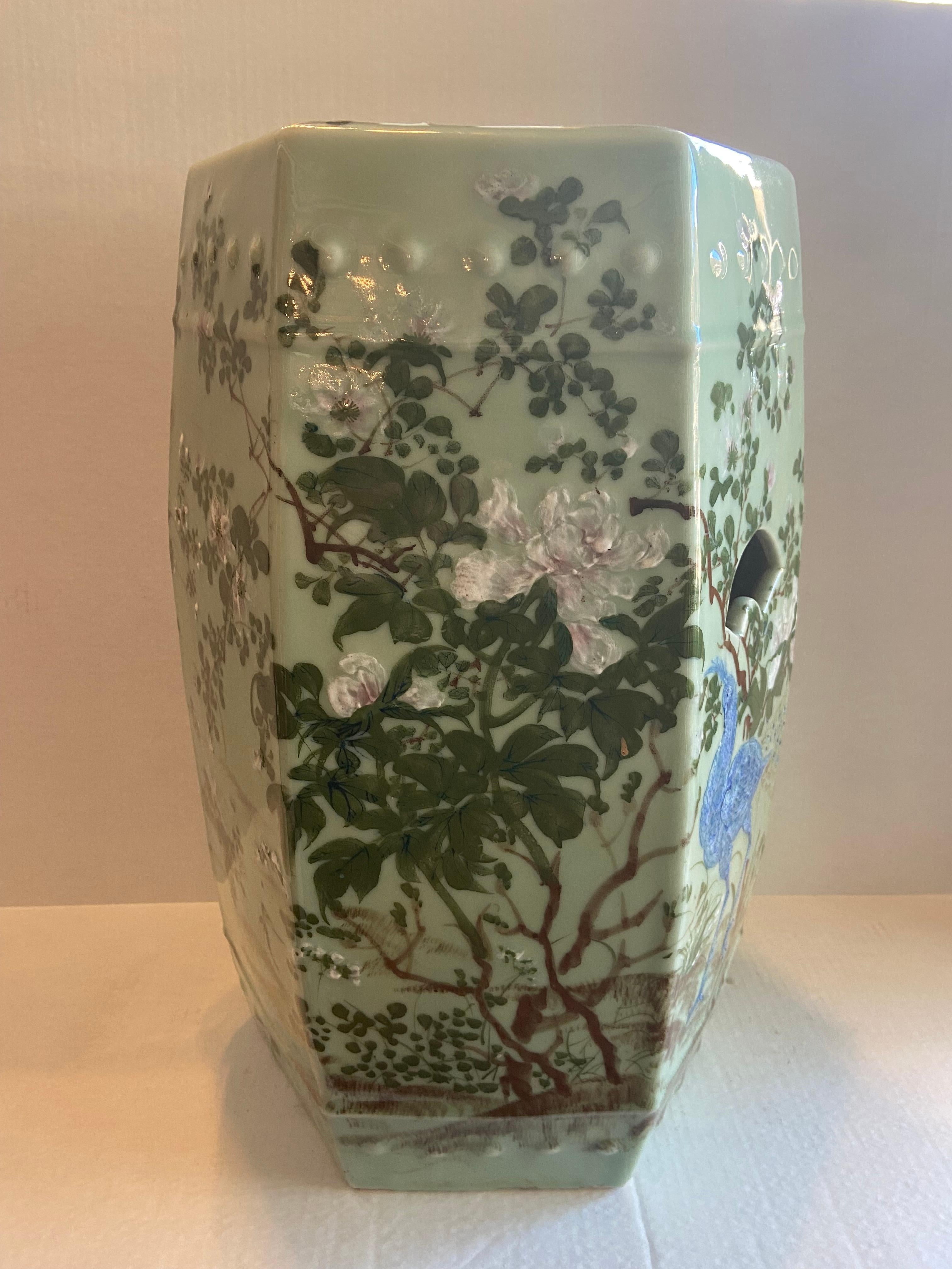 Japanese Antique enameled porcelain and celadon glazed garden stool with under-glaze blue peacock surrounded by floral decoration in pink and white flowers blooming from green leaved branches with fan shape opening for handles, circa 1900.