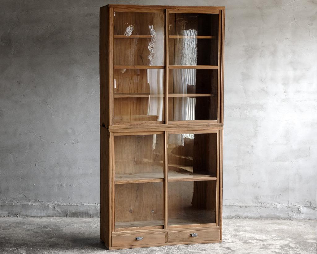 This antique glass sliding door cupboard crafted in the Taisho Era(1912-1926).

It features slender lines and a delicate appearance, with subtle decorative elements on the front that enhance its beauty. The drawer pulls are also designed with