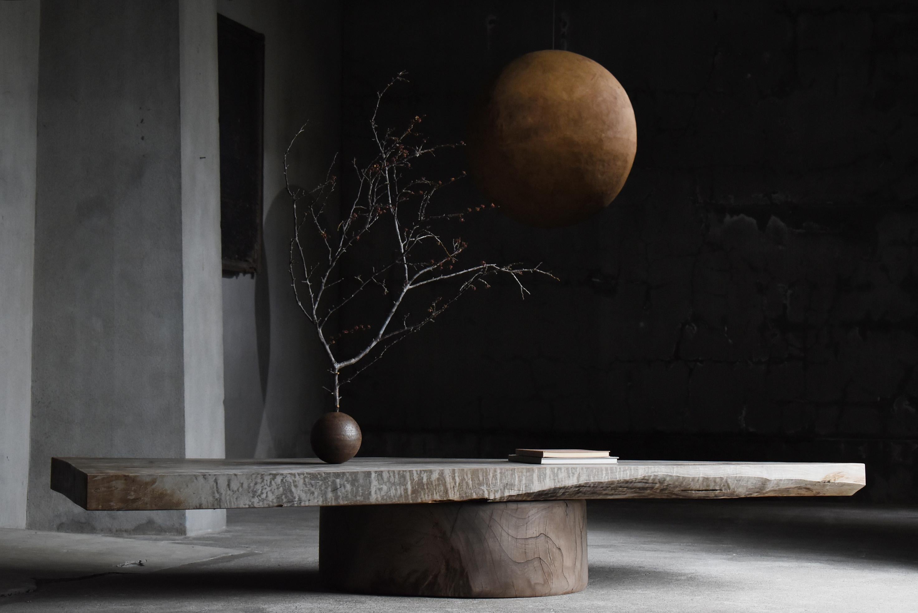 Se trata de una antigua y enorme mesa baja fabricada en Japón.
Presenta una estructura extremadamente sencilla pero potente, con una imponente placa superior de una sola pieza colocada sobre una base redonda que recuerda a un tocón. El tablero y la
