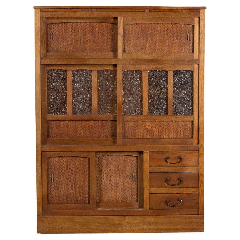 An antique Japanese kitchen cabinet from the early 20th century with sliding doors, drawers, woven rattan accents and textured glass panels. Created in Japan during the early years of the 20th century, this kitchen cabinet features a linear