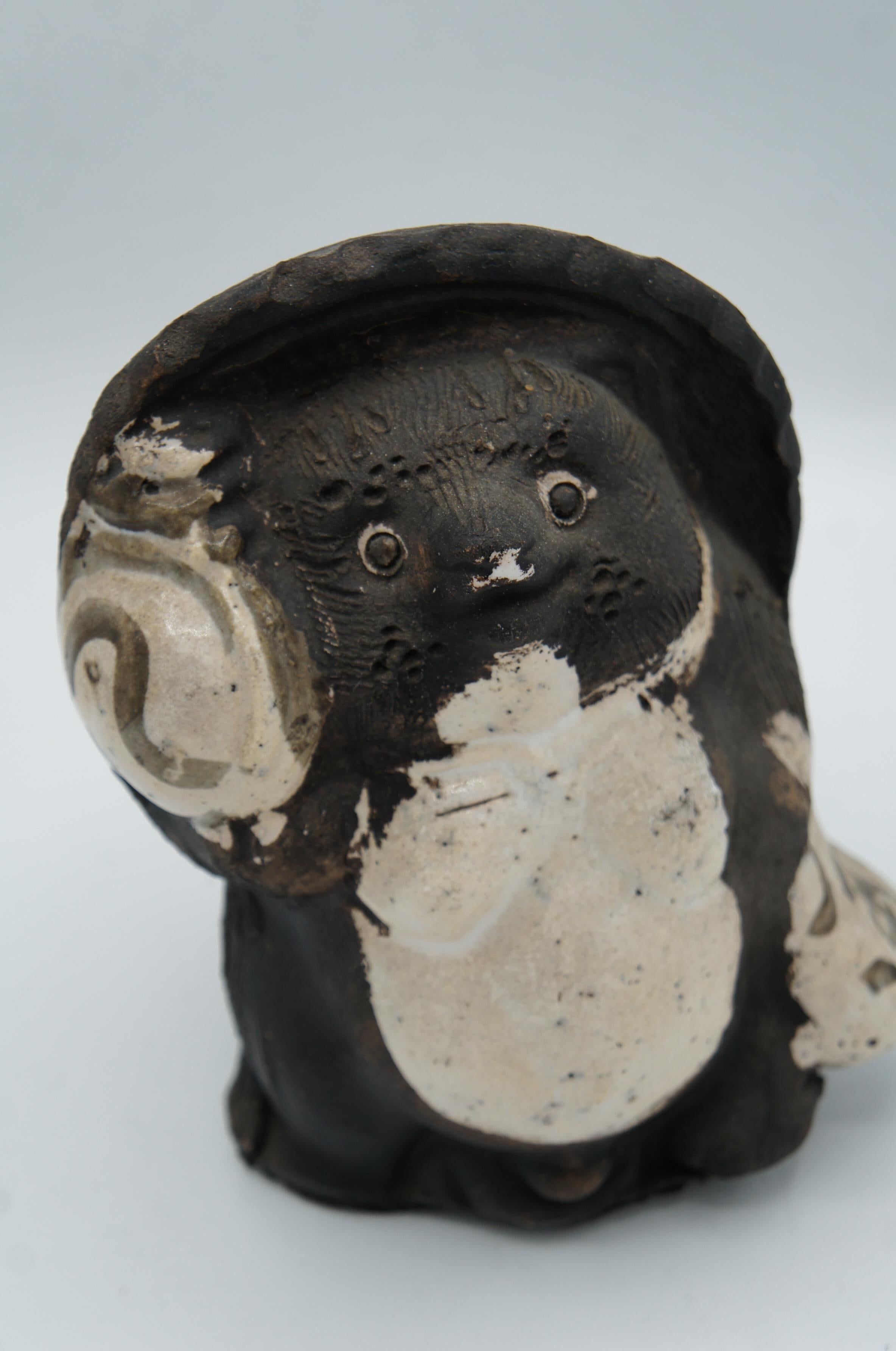 This is an object called 'Shigaraki Tanuki' which was made around 1960s.
It was made in a town called Shigaraki in Shiga prefecture in Japan.
It is made with porcelain. Tanuki is a Japanese racoon and it has 8 fortunes meanings.

1)The Hat: The