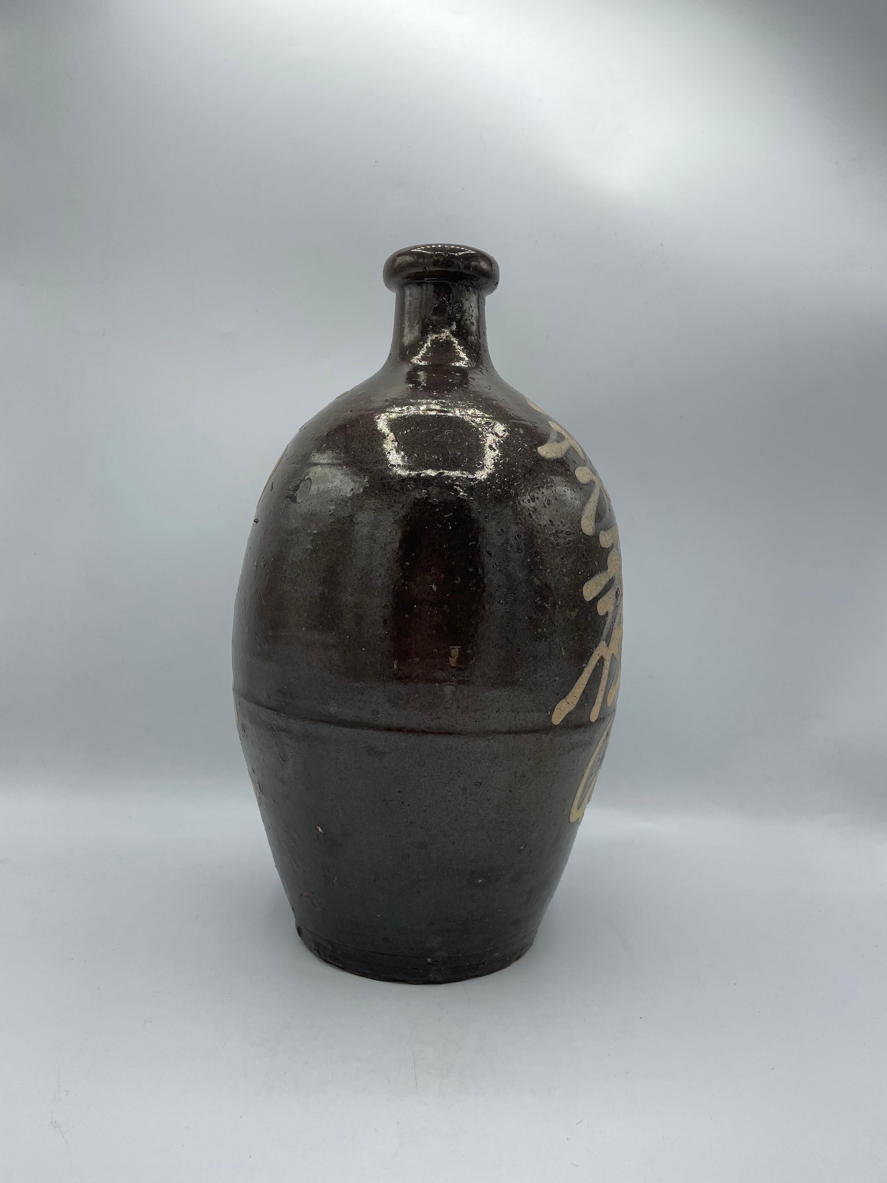 This is a sake bottle called 'Kayoi tokkuri' or 'Binbo tokkuri'. It is made with a porcelain and it is written Manazuru-machi and Fukubi.
Manazuru-machi is the city name and it is located in Ohita prefecture.
This bottle was made in Japan around