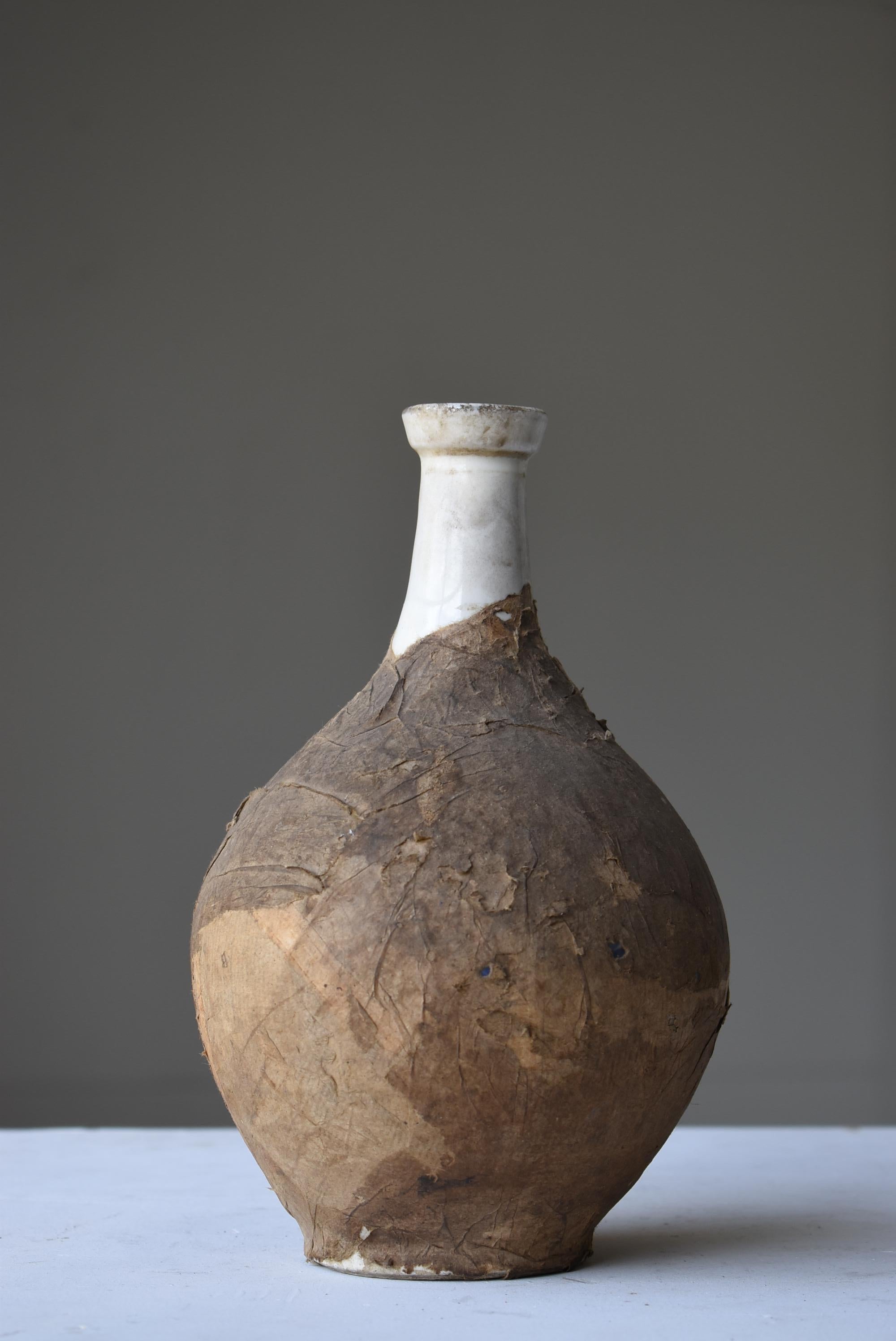 This is an old Japanese sake bottle.
It is from the Meiji period (1860s-1900s).
It is made of ceramic and covered with paper.

It is slightly cracked and reinforced with paper.

The paper is peeling off in places, giving it the beauty of an abstract