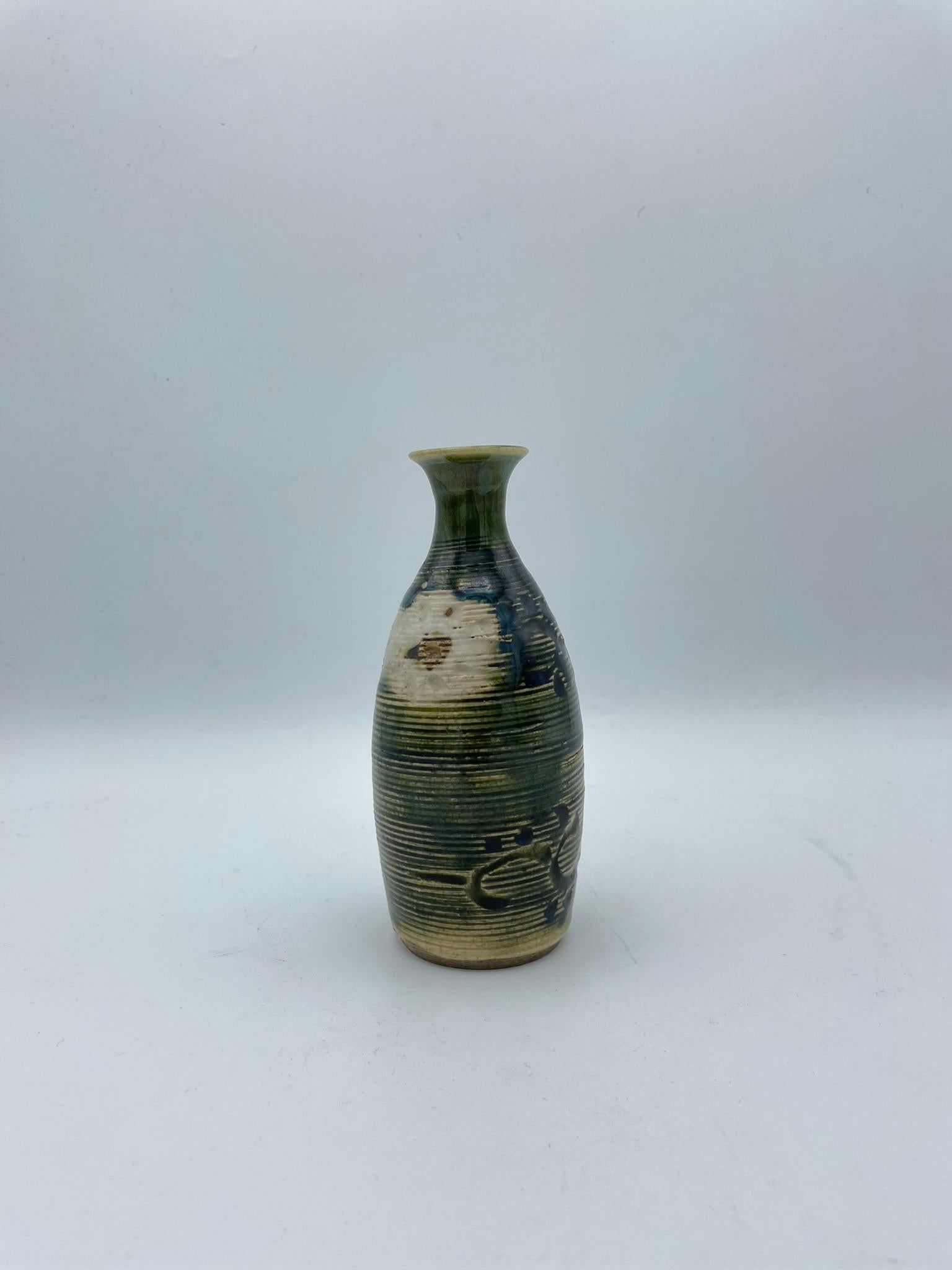 Dies ist eine Flasche für Sake, die auf Japanisch 'Tokkuri' heißt.
Diese Tokkuri wurde in der Meiji-Ära um 1900 hergestellt.
Es ist aus Porzellan und im Oribe-Stil (Oribe ware/ Oribe yaki) gefertigt.

Der japanische Keramikstil 