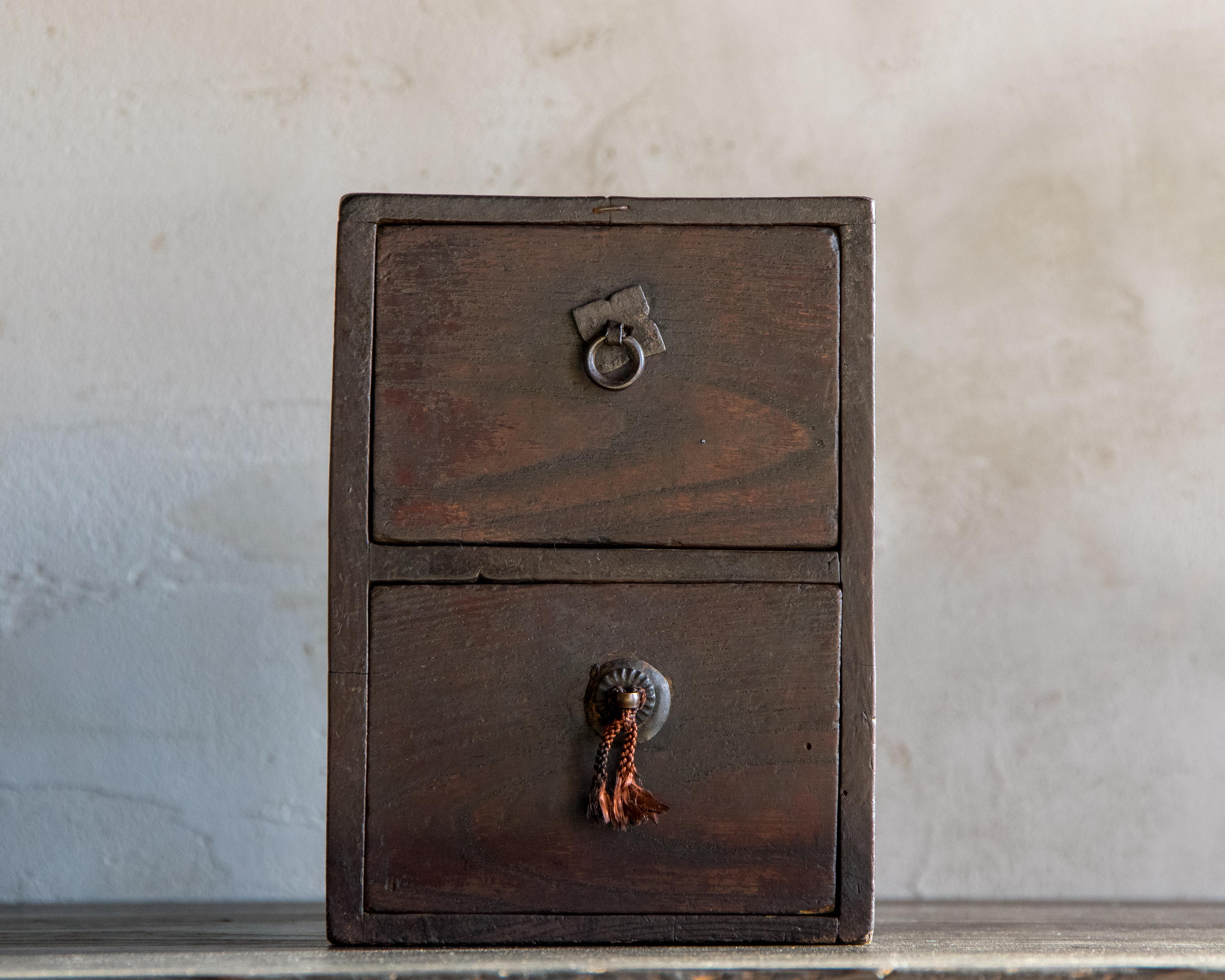 Ce petit coffre ancien a été fabriqué à l'ère Meiji (1868-1912) en keyaki (zelkova japonais), un bois dur dense et expressif connu pour sa durabilité et sa surface chaleureuse. Compact mais imposant, il est doté d'une simple poignée en métal sur le