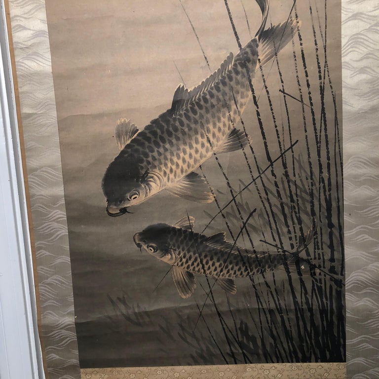 Japan, a pair of old 19th century Koi or Carp depicts a mature fish and its smaller youthful off spring - both ripple the waters among the reeds in this auspicious art composition. It is a hand painting on paper scroll dating to the Taisho period,