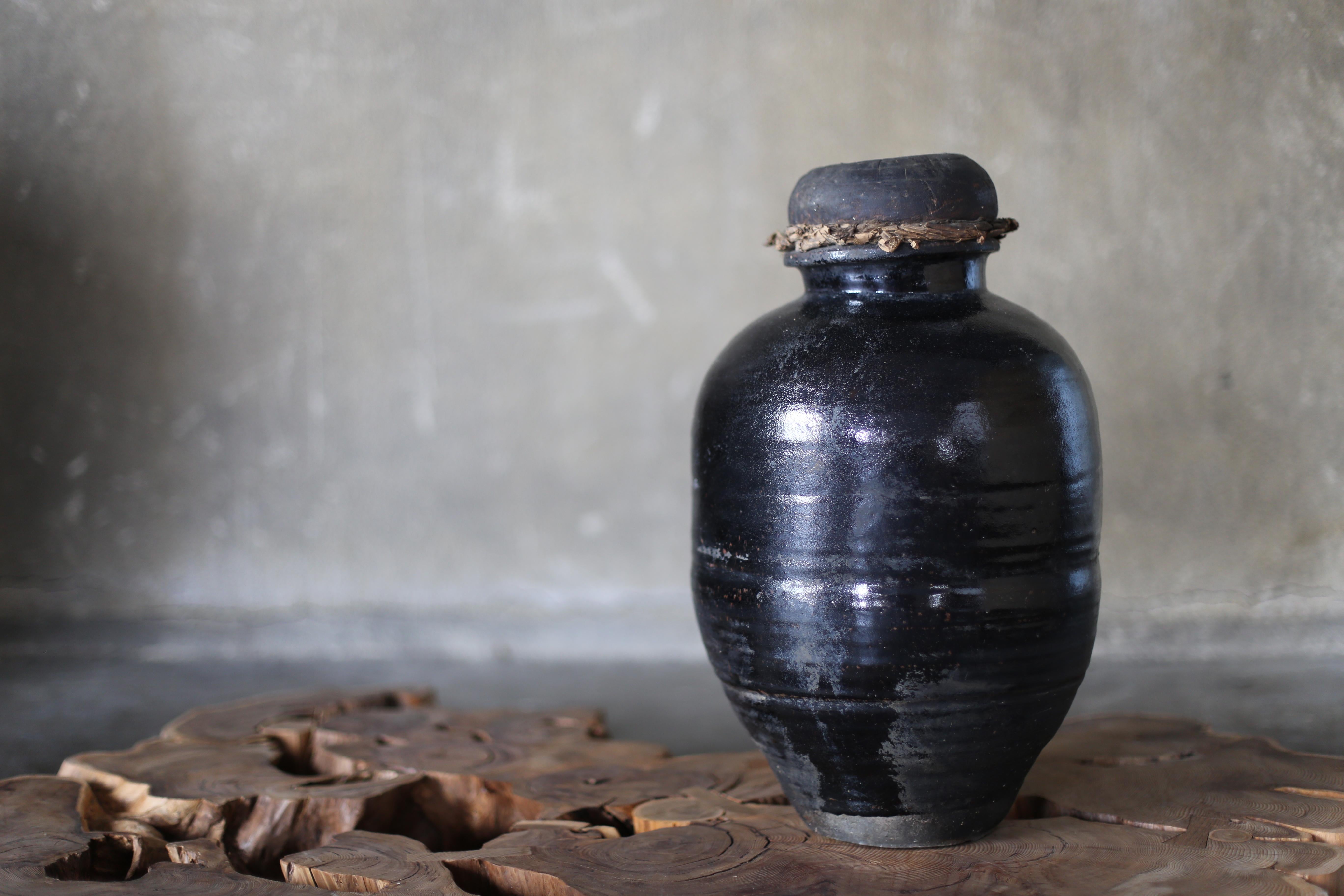 This ancient ceramic jar was once used as a storage container in Japanese homes and merchant houses.
It is coated with a deep, lustrous black glaze, which has developed a subdued luster and crazing over time. Its soft, rounded form and the