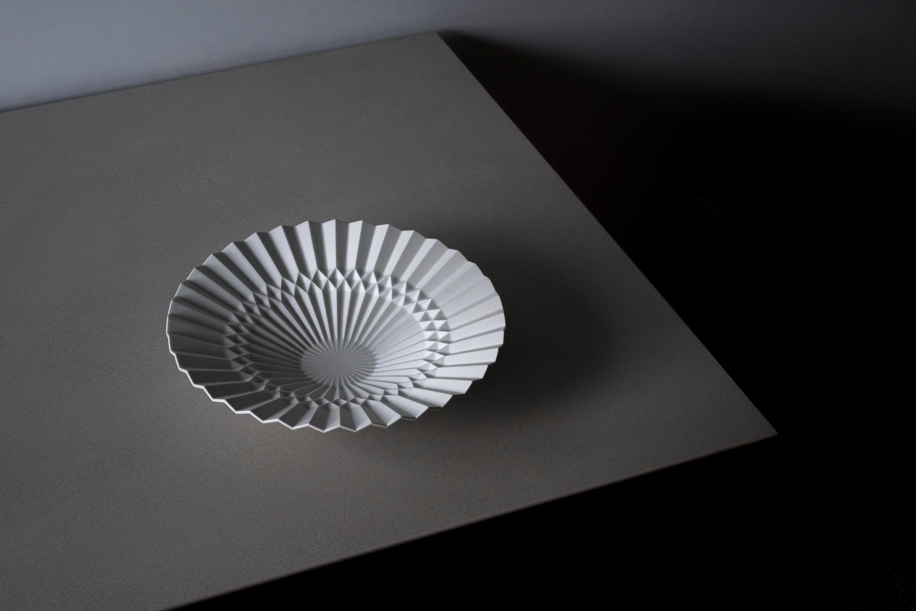 Ce plateau est conçu par Denis Guidone et fabriqué à la main au Japon par Risogama pour Hands on Design, une poterie traditionnelle. Rappelant la tradition japonaise de l'Origami, le designer utilise la porcelaine blanche Arita comme du papier et