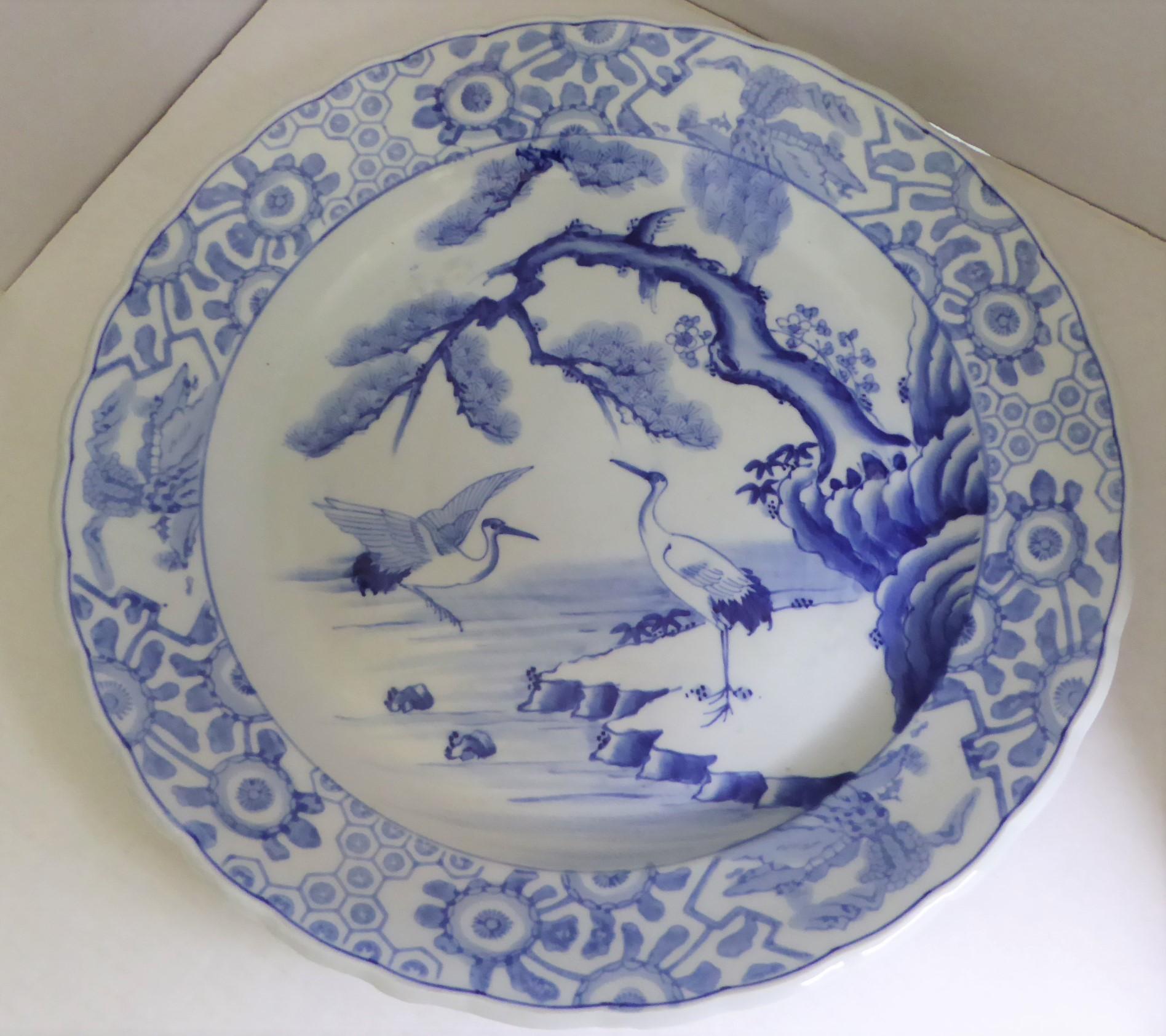 Beautiful Meiji period blue and white Japanese Imari Charger depicting a standing crane or stork under a pine tree at water's edge and another coming back for a landing. Two stylized turtles are seen swimming nearby. Rim decorated with 3 medallions