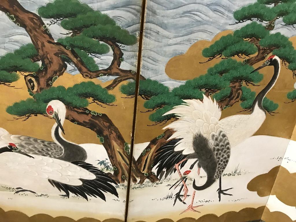 A magnificent six panel Japanese Byobu folding screen (likely Meiji Period but possibly Edo period) depicting cranes at play near the ocean shoreline. Crashing waves and large juniper trees give the image a rather unique feel. The colors and gold