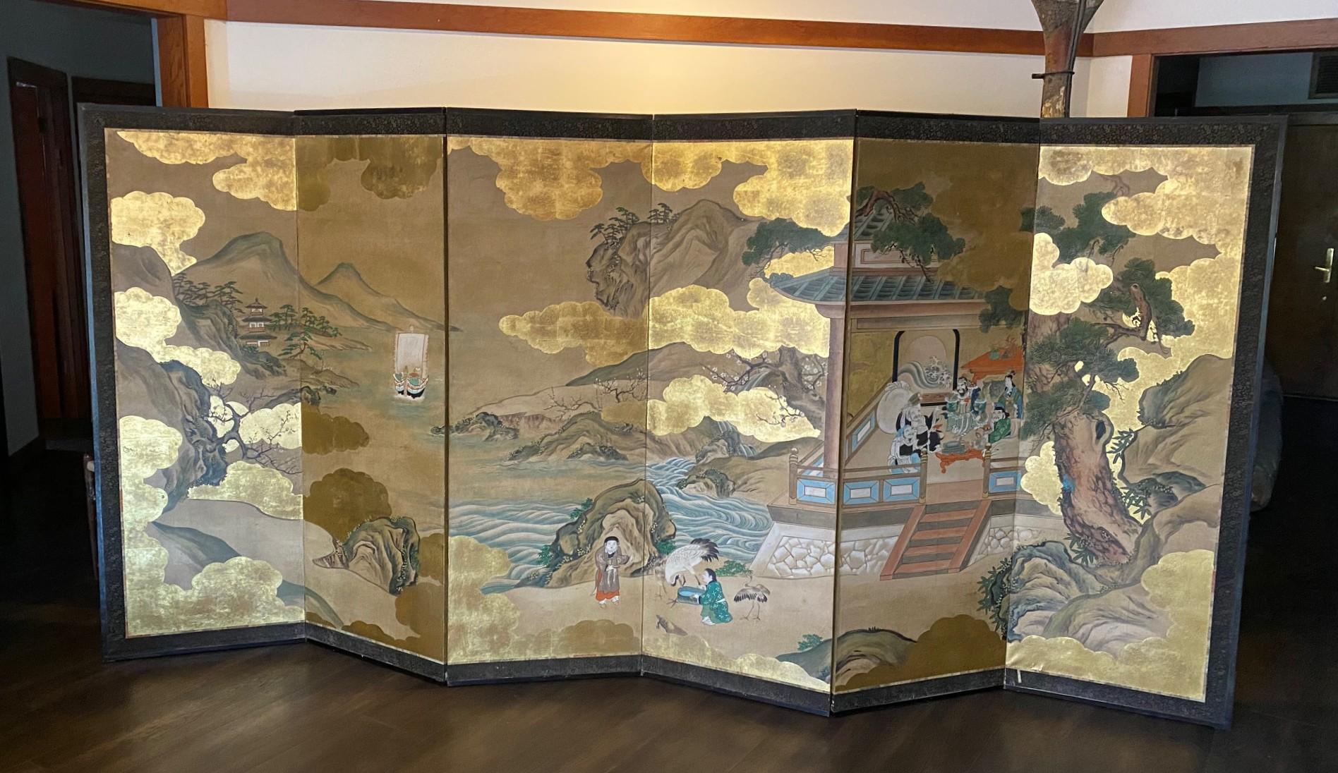 Magnifique paire de paravents Byobu japonais/asiatique à six panneaux, peints à la main, représentant une scène de village presque magique/mythique avec des nuages dorés flottants (rehaussés de feuilles d'or et de poussière d'or), de grands arbres