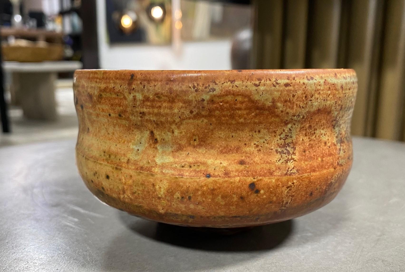 A gorgeous Japanese studio pottery chawan tea bowl that features a wonderful reddish-orange glaze with various shifts in colour and texture. 

This particular piece encompasses the Japanese Wabi-Sabi aesthetic (which is so revered and coveted in