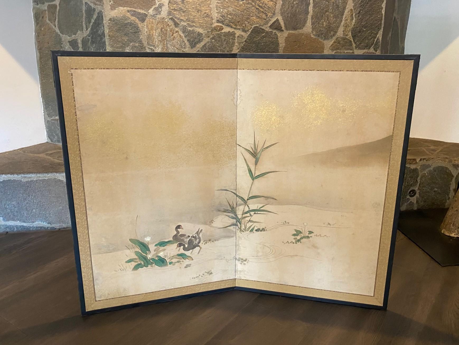 Magnifique paravent japonais Byobu à deux panneaux représentant un paysage naturel avec deux oiseaux sauvages s'ébattant au bord d'une rivière ou d'un lac parmi des fleurs épanouies.  La composition, les magnifiques détails peints à la main et