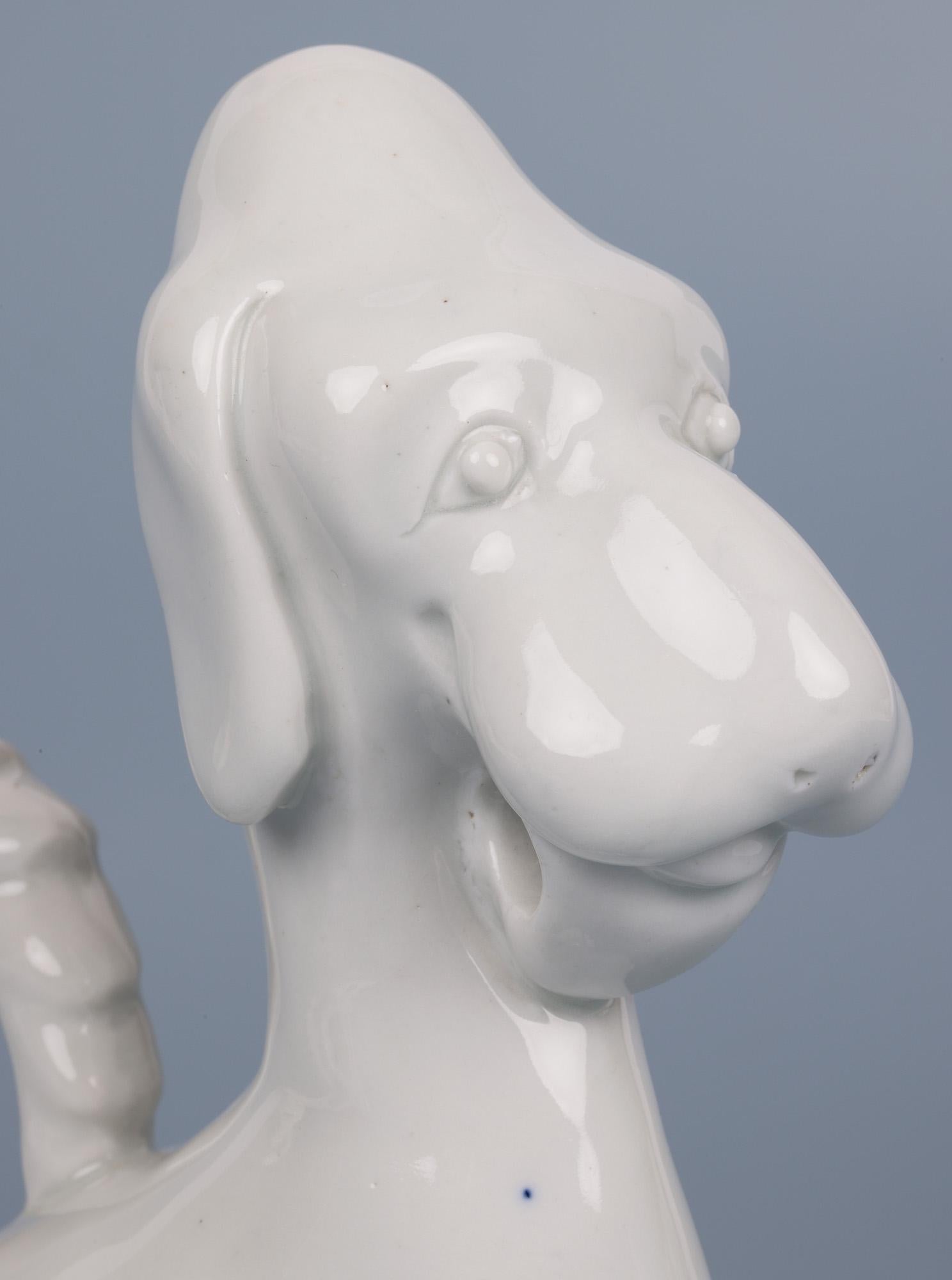A fine Japanese attributed Blanc De Chine porcelain model of a amusing stylized dog dating from the early 20th century. This interesting figure is modelled as a seated dog with its tail looped and forming a handle and with an open loop below its