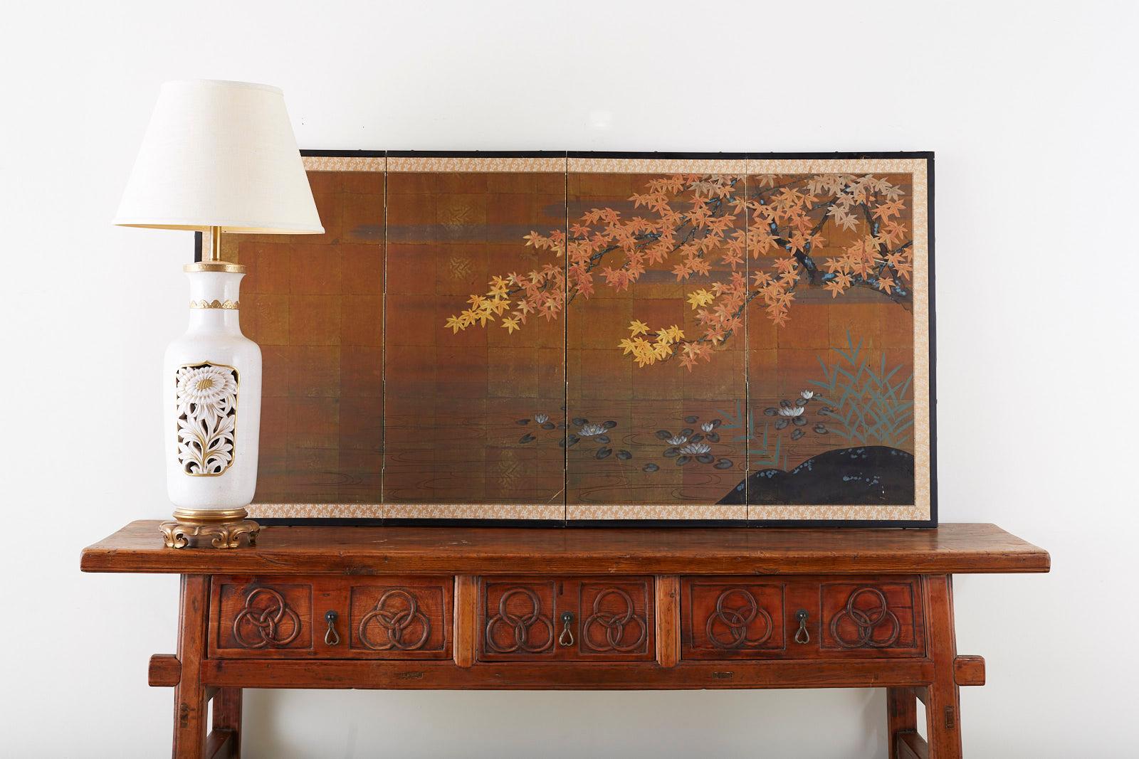 Serene Japanese four-panel byobu screen depicting a seasonal nature scene of an autumn maple tree over a pond with lily pads. Painted in a Rinpa school style over a background of gilt squares and set in a black lacquered frame with a contrasting