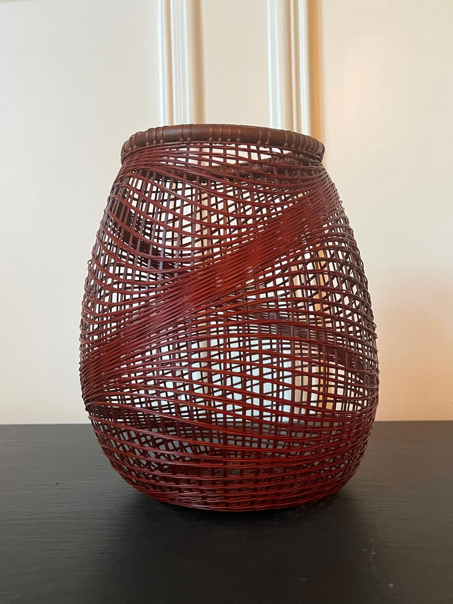 A Japanese Ikebana bamboo basket woven by artist Abe Motoshi (Japanese, b. 1942). Constructed with lacquered reddish Madake bamboo and rattan with technique of open and irregular twinning, the basket features an organic form with undulating woven