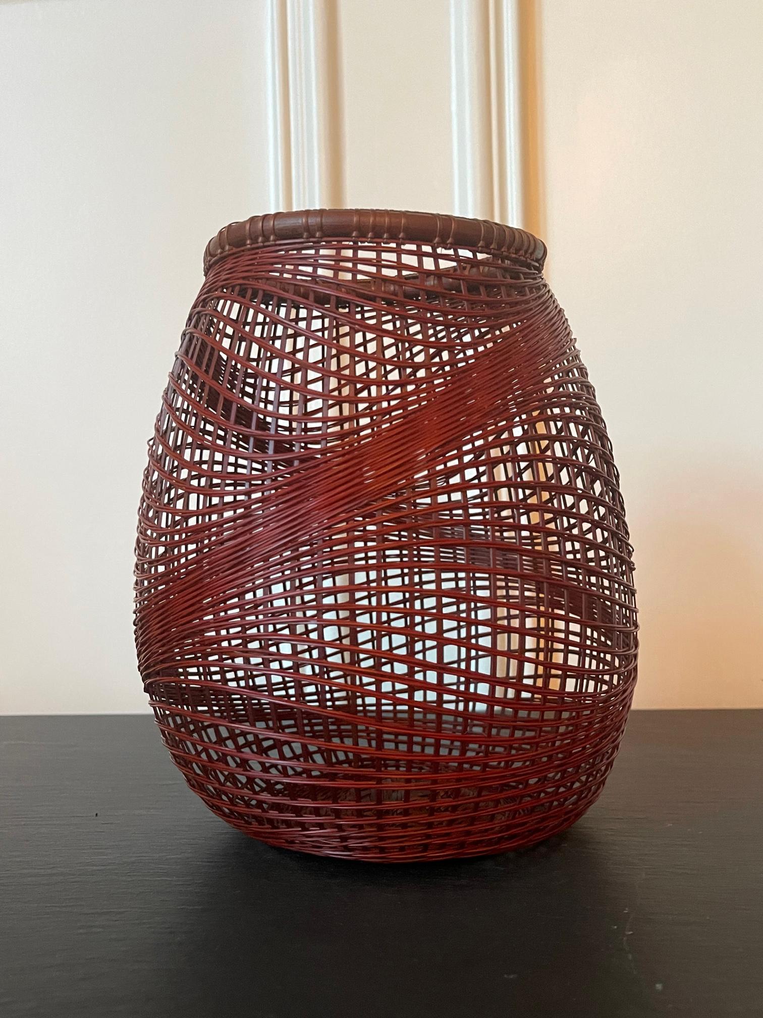 Ein japanischer Ikebana-Bambuskorb, geflochten vom Künstler Abe Motoshi (Japaner, geb. 1942). Der aus rötlich lackiertem Madake-Bambus und Rattan in offener und unregelmäßiger Flechttechnik gefertigte Korb weist eine organische Form mit wellenförmig