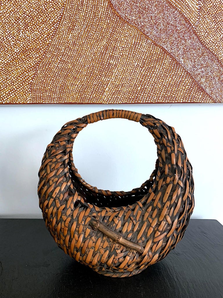 A Japanese woven bamboo basket in the shape of crescent with open top and a wrapped handle circa 1920s-1940s. The basket was woven with 
