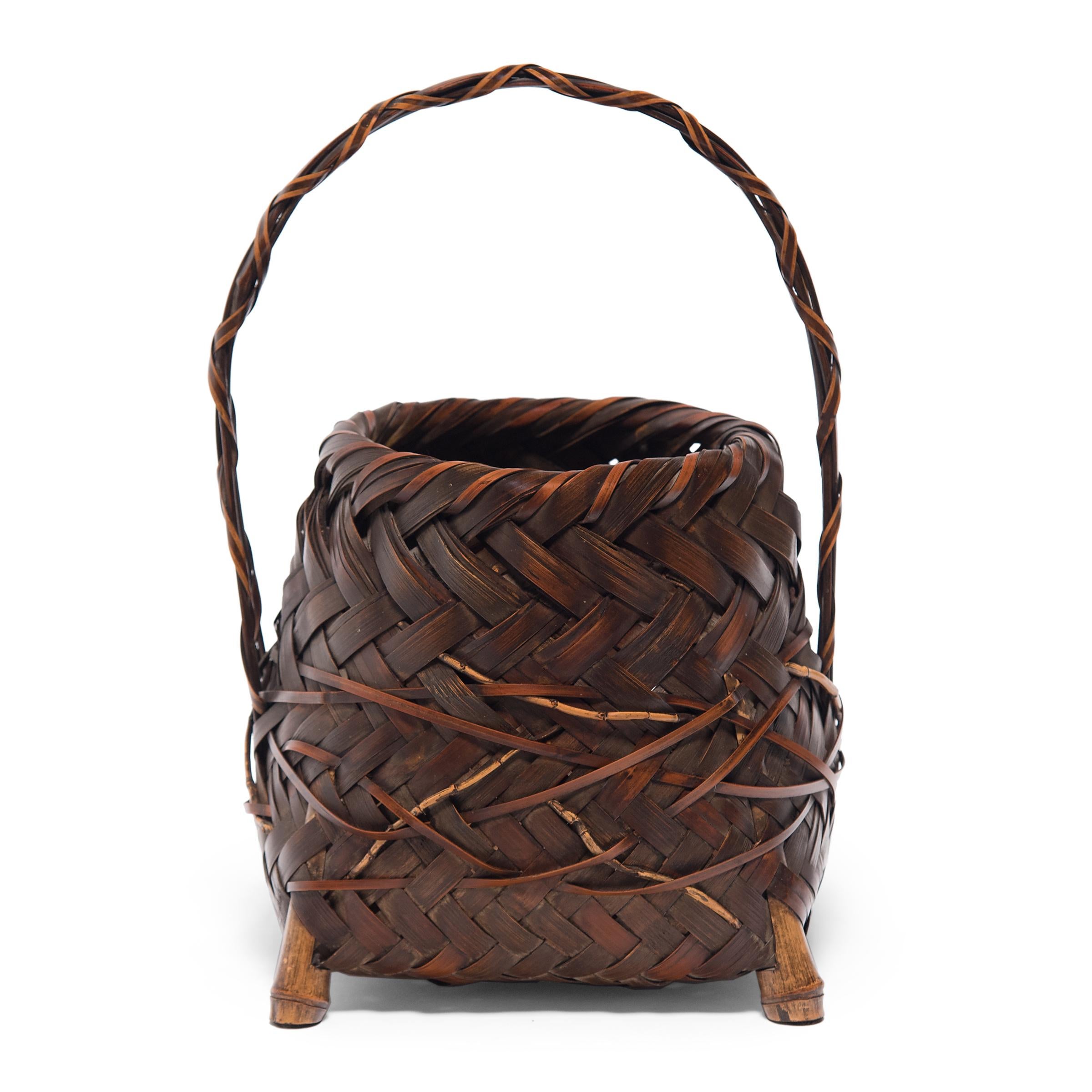 This one-of-a-kind bamboo basket is a late-Meiji era flower basket (hanakago) designed especially for ikebana, the Japanese art of floral arrangement. The basket has a trapezoidal form that tapers to a round opening and is surmounted by a high,