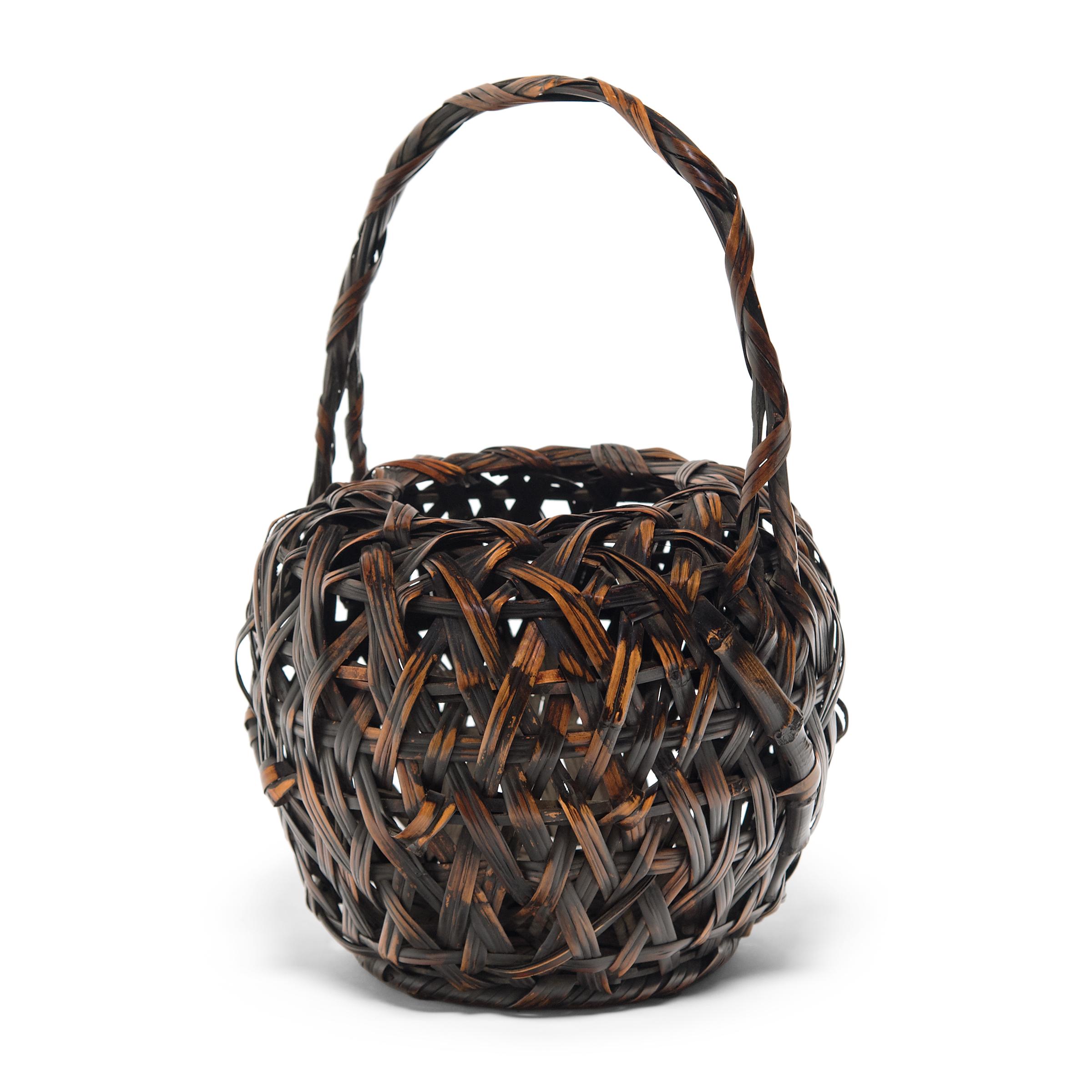 This one of a kind bamboo basket is a late-Meiji era flower basket (hanakago) designed especially for ikebana, the Japanese art of floral arrangement. The basket has a rounded, barrel form and a high, arched handle. The body of the basket is loosely