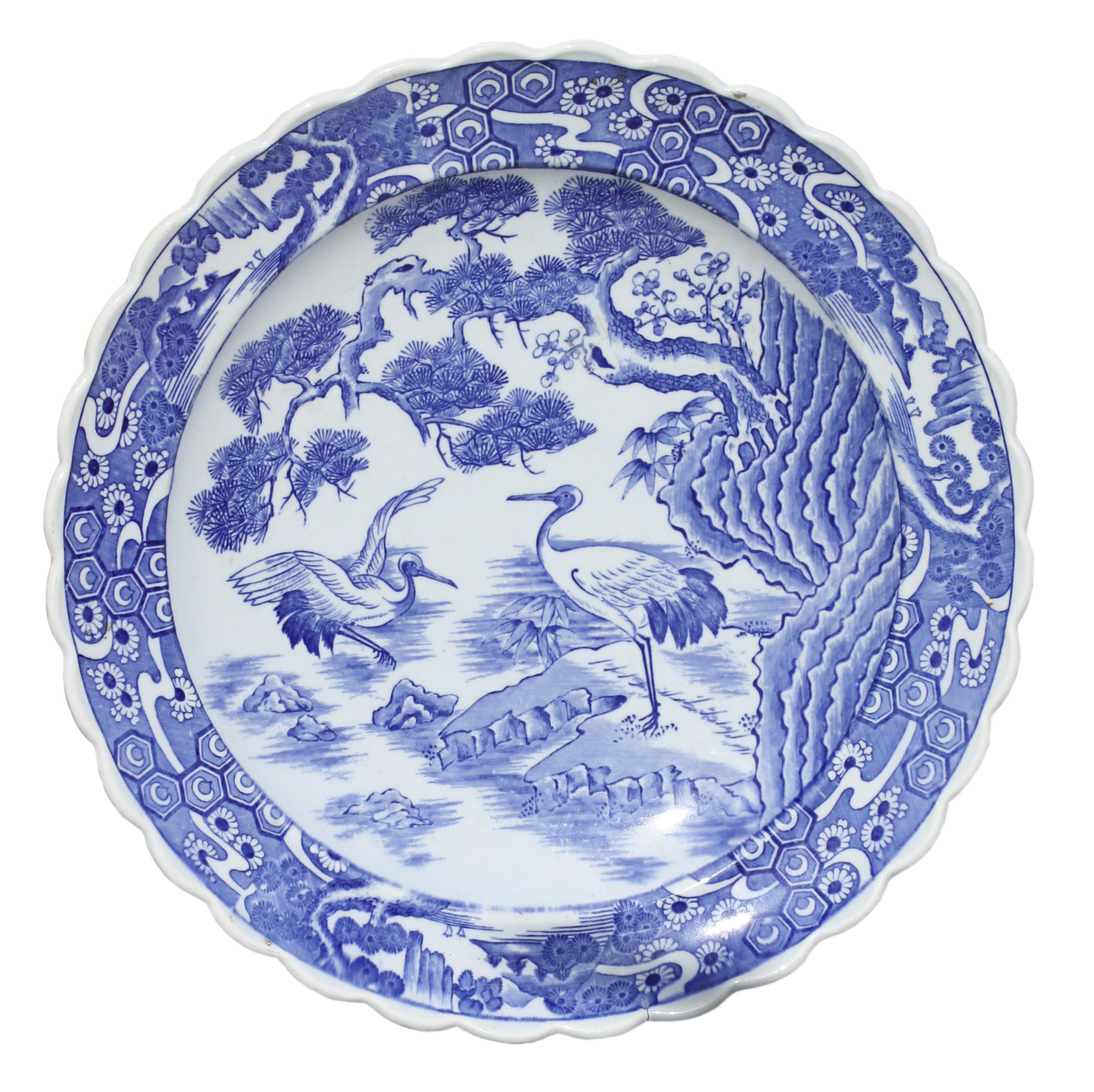 
JAPANESE BLUE AND WHITE DECORATED PORCELAIN PLATE, MEIJI PERIOD (1868-1912)
the underside with impressed signature, with a tightly scalloped edge, border of stylized motifs, the center recess representing two cranes in a stylized marsh.

Diameter