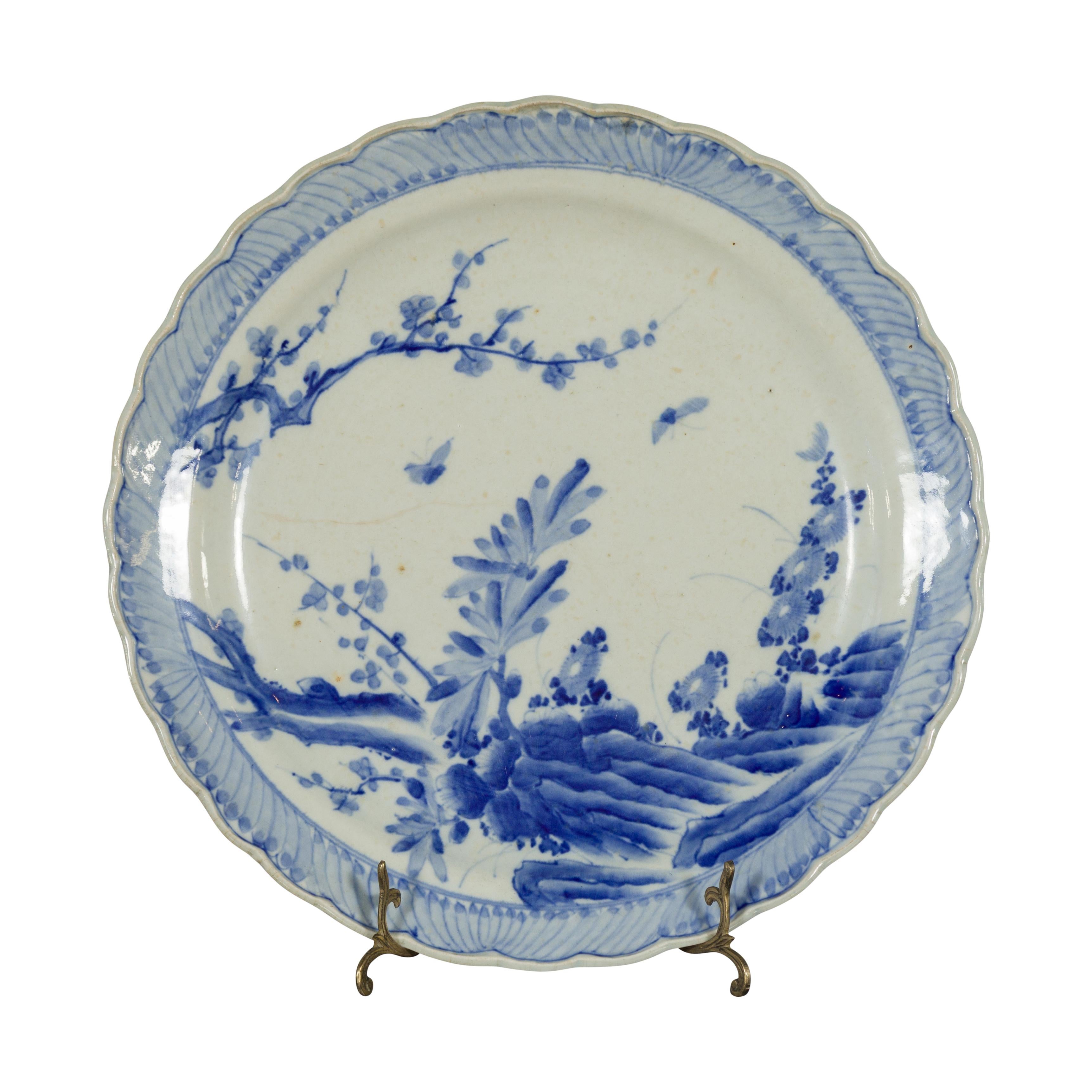 Ein japanischer Porzellanteller aus dem 19. Jahrhundert mit handgemaltem blau-weißem Dekor aus blühenden Bäumen, Blumen und Schmetterlingen. Dieser Porzellanteller, der im 19. Jahrhundert in Japan hergestellt wurde, zeigt ein zartes blau-weißes