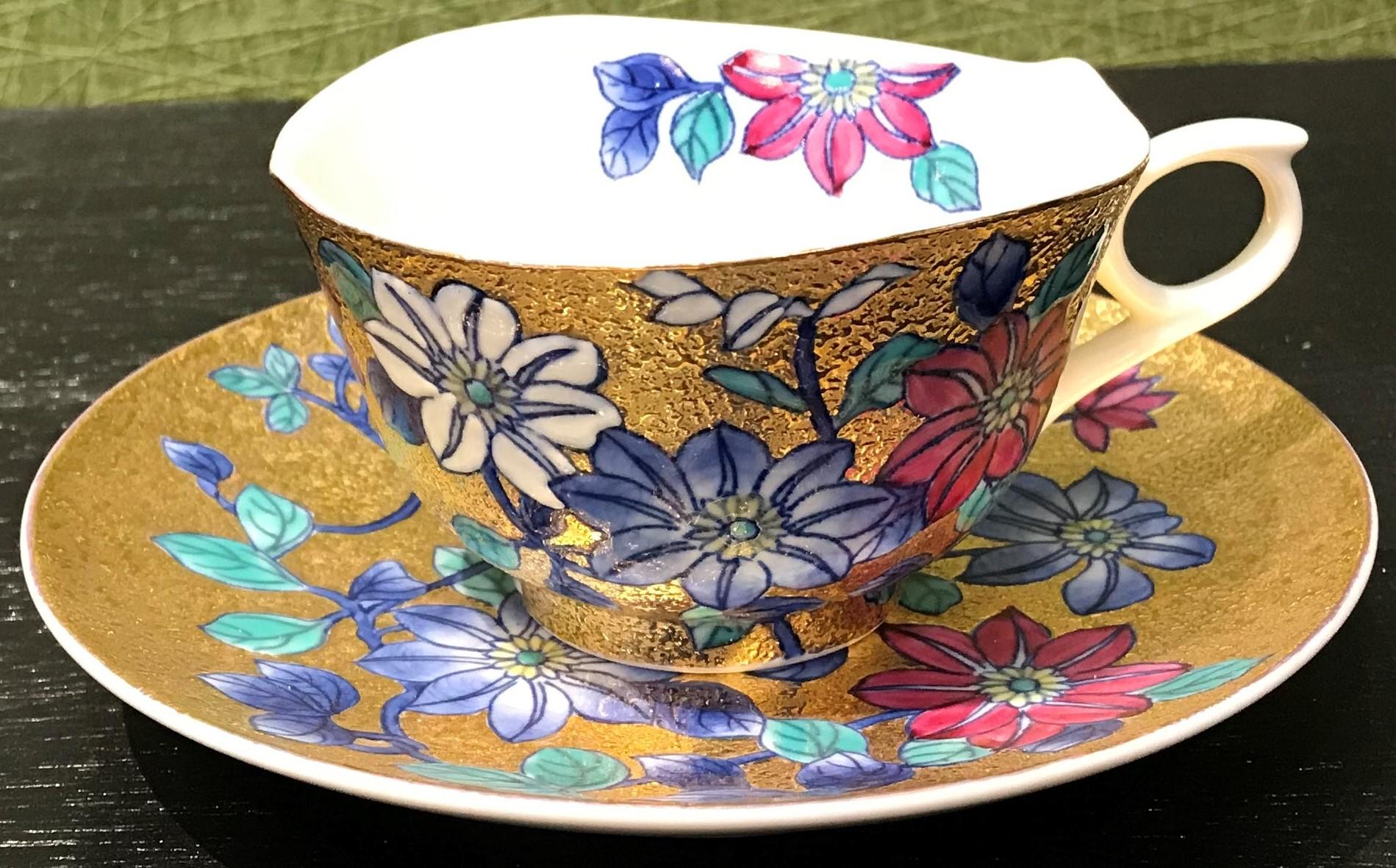 Striking contemporary gilded fine porcelain cup and saucer, intricately hand painted in vivid blue and red and white on an attractive gilded body, featuring stunning clematis flowers in full bloom. This cup and saucer is from a signature series by a