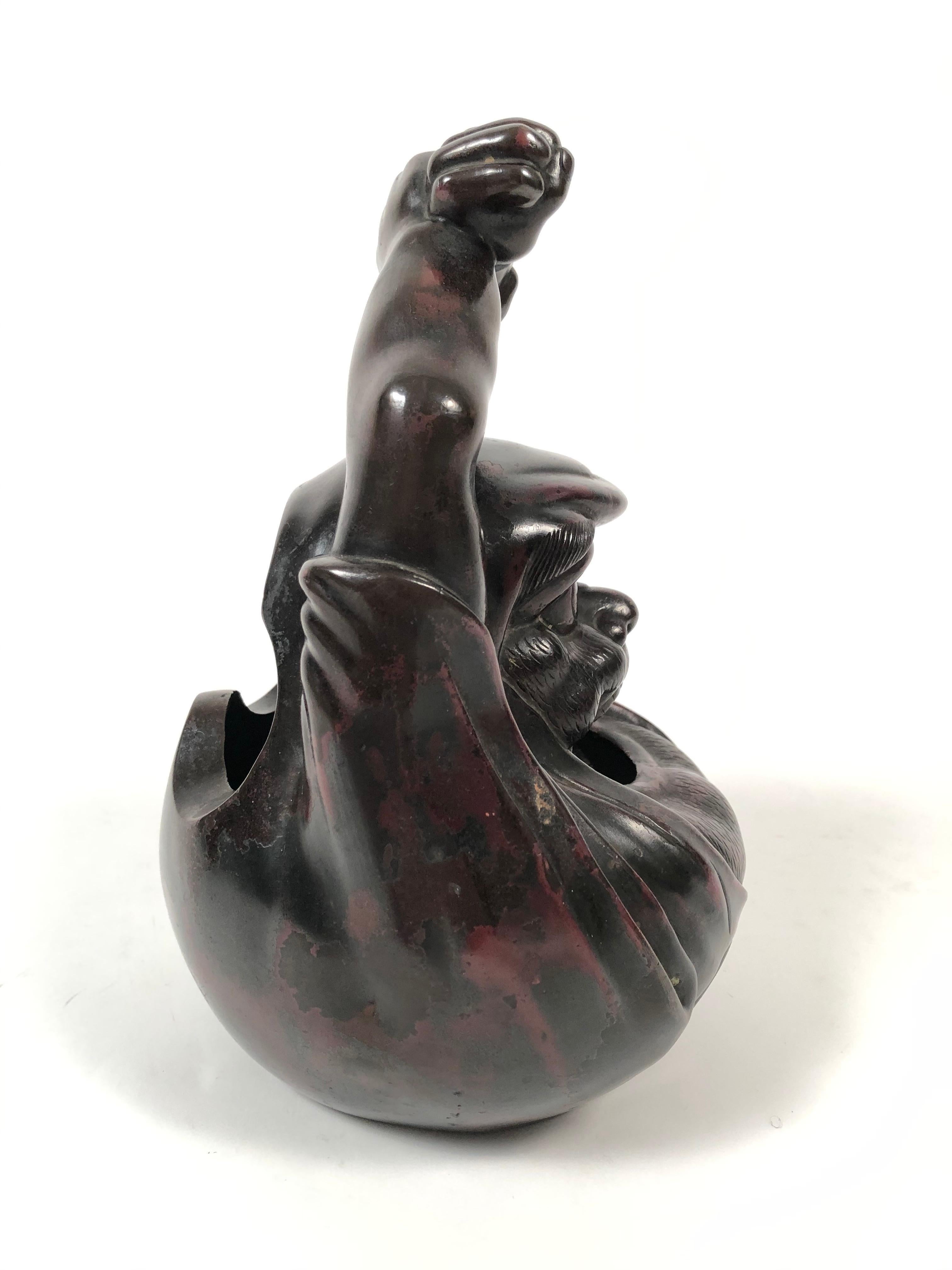 A 19th century Meiji period Japanese bronze brazier, in the form of Bodhidharma or Daruma, as he is known in Japan, designed to be used as a hand warmer, with his arms raised above his head and hands interlocked to form a carrying handle. Coals