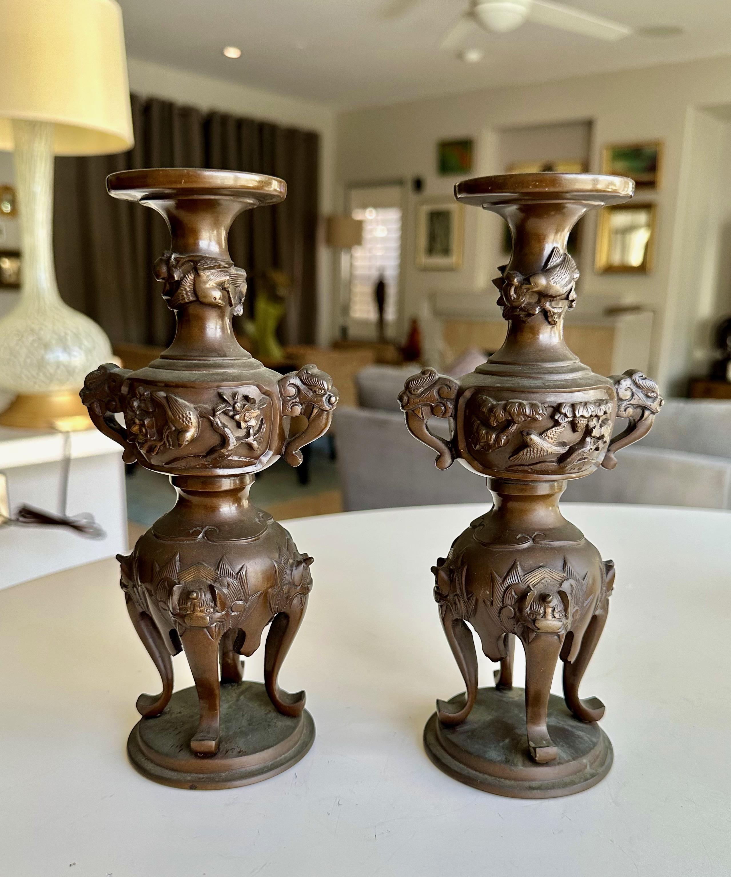 A pair of vintage Japanese bronze candlesticks with elephant head handles, adorned with finely chased birds and plants. 