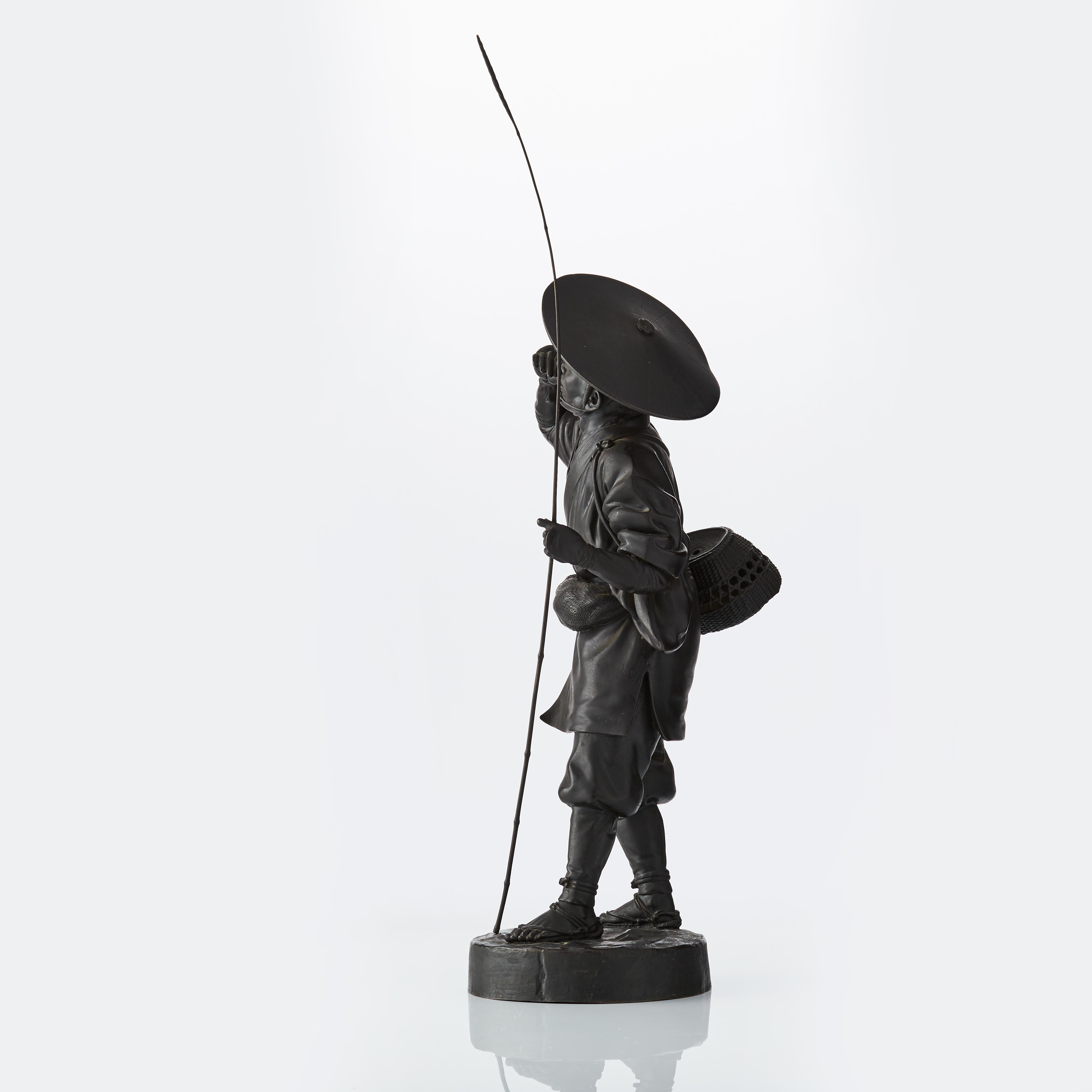 A Japanese bronze figure of a fisherman standing in a relaxed stance, head tilted up and to the left, gazing to the distance, cigarette raised to the mouth in the right hand, the left grasping a tall thin fishing rod, wearing a conical kasa atop the