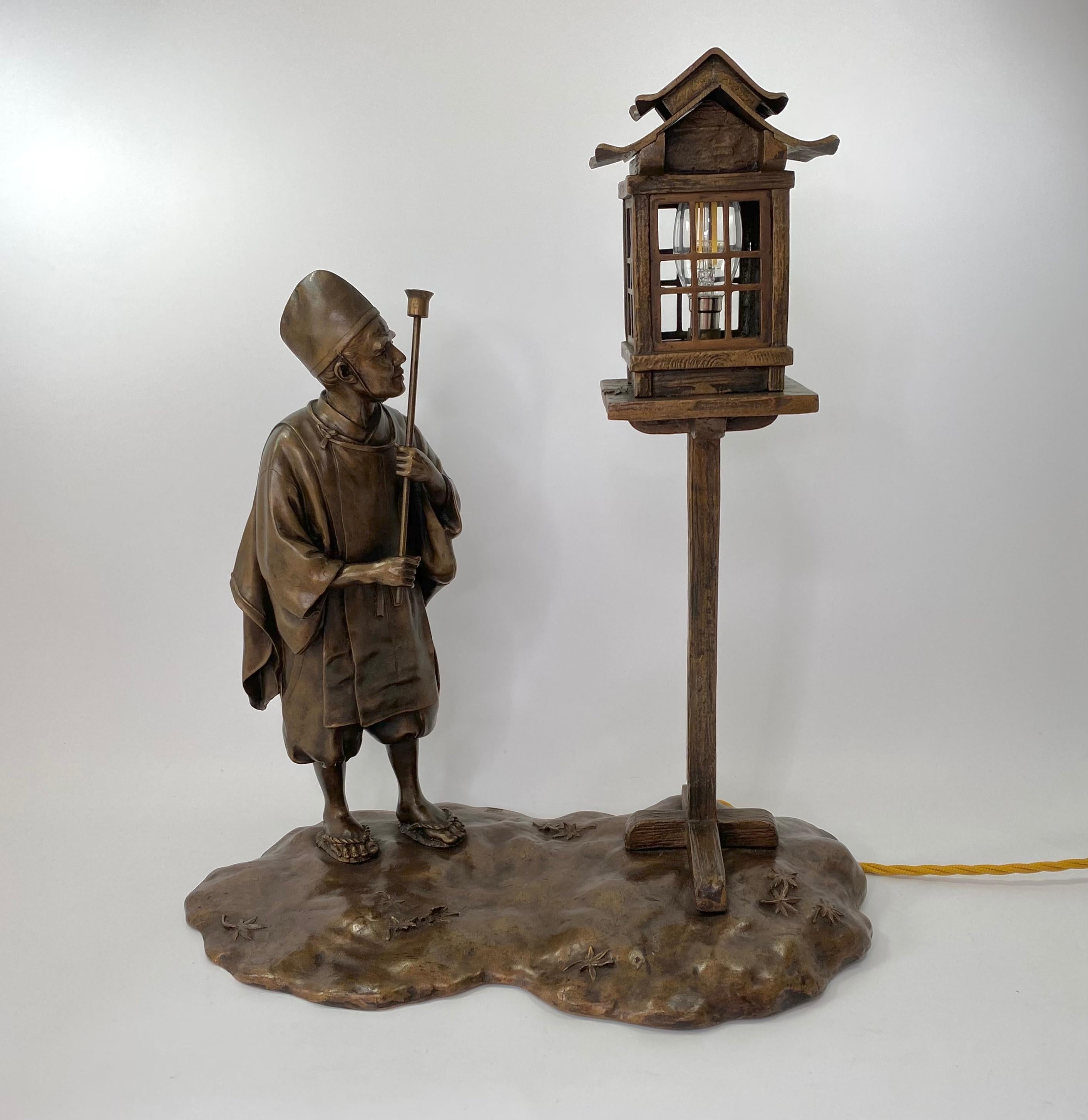 A fine Japanese bronze okimono lamp, signed Yoshitani,
????. c.1900, Meiji Period.
Modelled as a lamp lighter, holding a torch, whilst preparing to light a pagoda topped lamp, which is supported atop a wooden pedestal.
The shaped base cast with