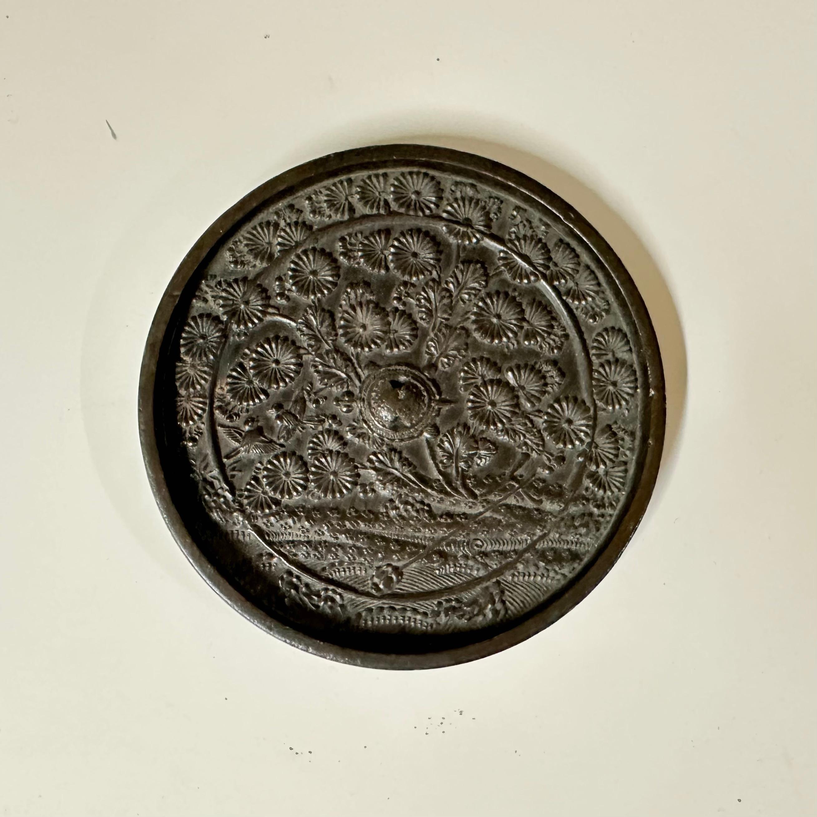 Questo squisito specchio giapponese in bronzo, che misura circa 11 cm di diametro, è un pezzo di storia raro e incantevole. Risalente al XIX secolo o anche prima, presenta una superficie dal design intricato ornata da un motivo floreale, che mette