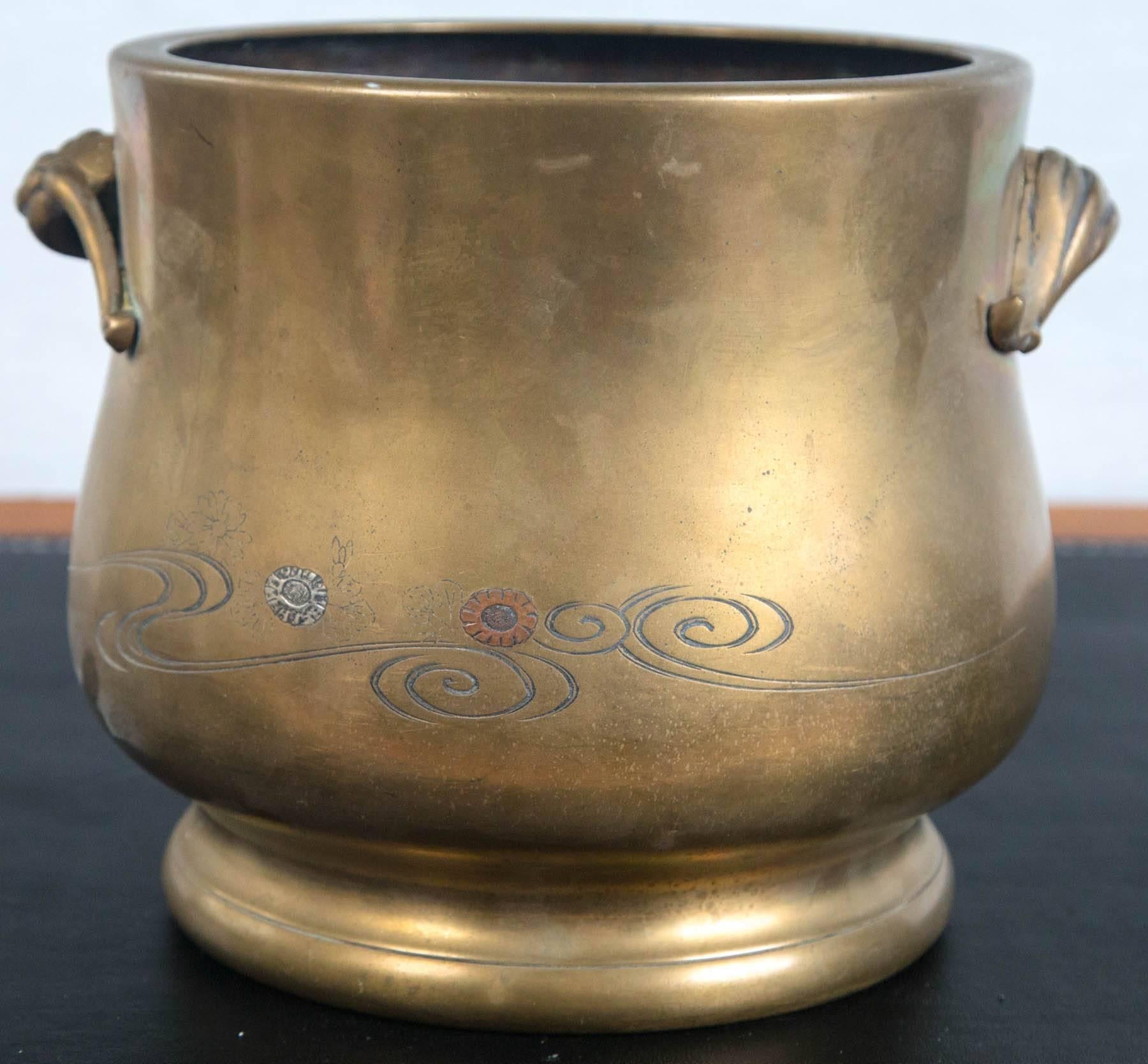 Runde Form mit Griffen in Form von Samenkapseln oder Blüten. Mit Silber- und Kupferelementen eingelegt, in Blümchen- und Wirbelmuster. Der Körper schwillt über der Basis an.
