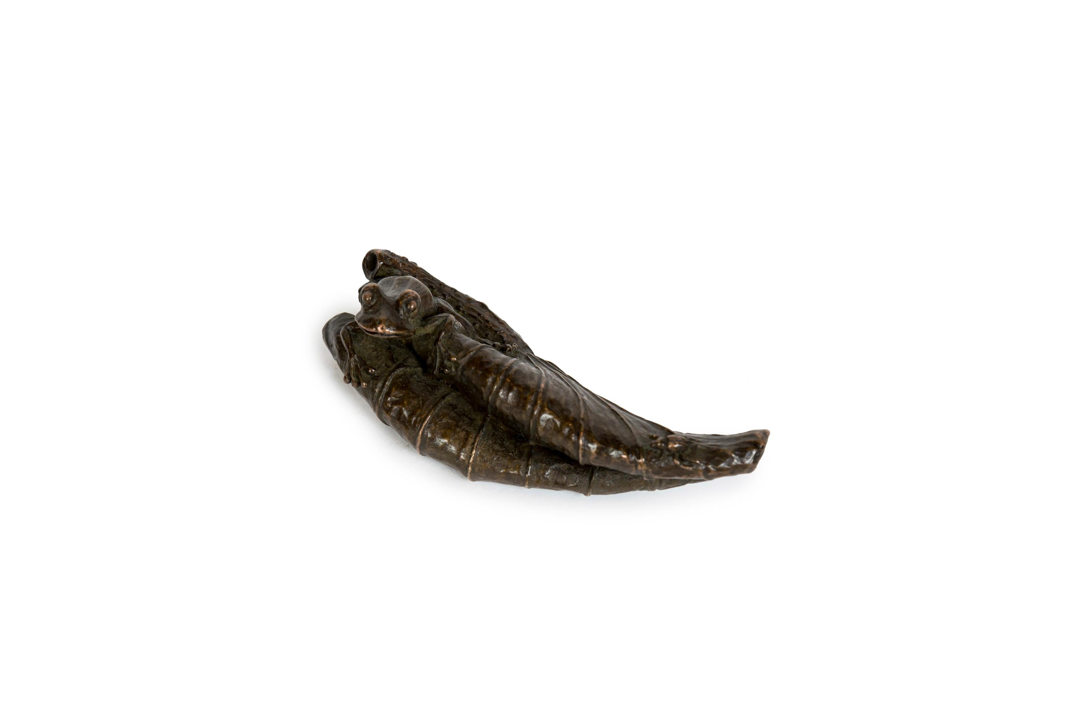 Una piccola scultura in bronzo di una rana che emerge da un'enorme foglia di loto, con un piccolo ma dettagliato scarabeo sull'altro lato della foglia. La rana (kaeru) è associata alla fortuna e alla ricchezza. Nel Giappone feudale, gli esattori