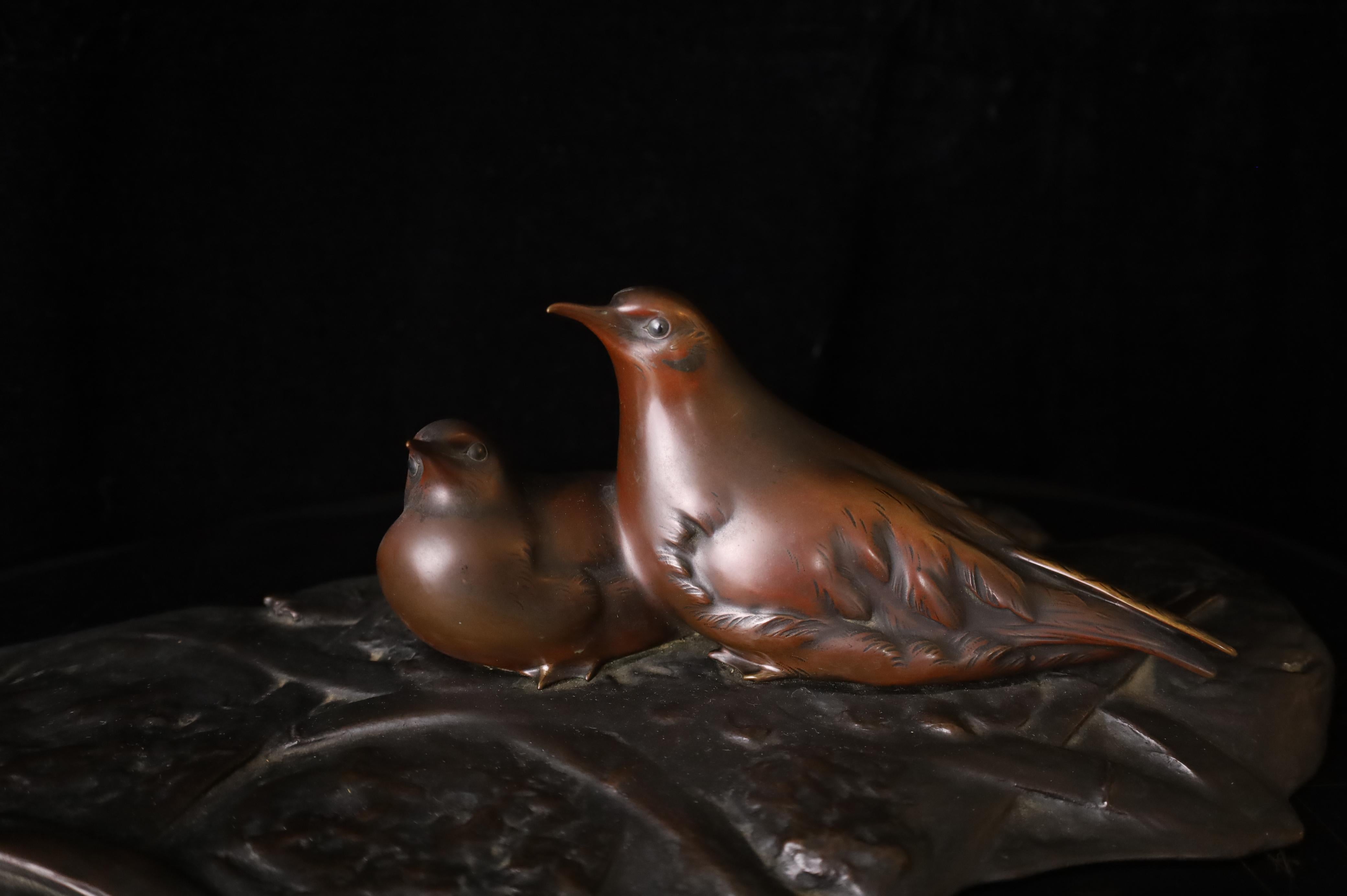 A serene and elegant Japanese bronze sculpture depicting a pair of birds resting on a large, naturalistically rendered leaf. Likely crafted during the Showa period, this piece showcases exquisite detail and patination, with soft reddish-brown hues