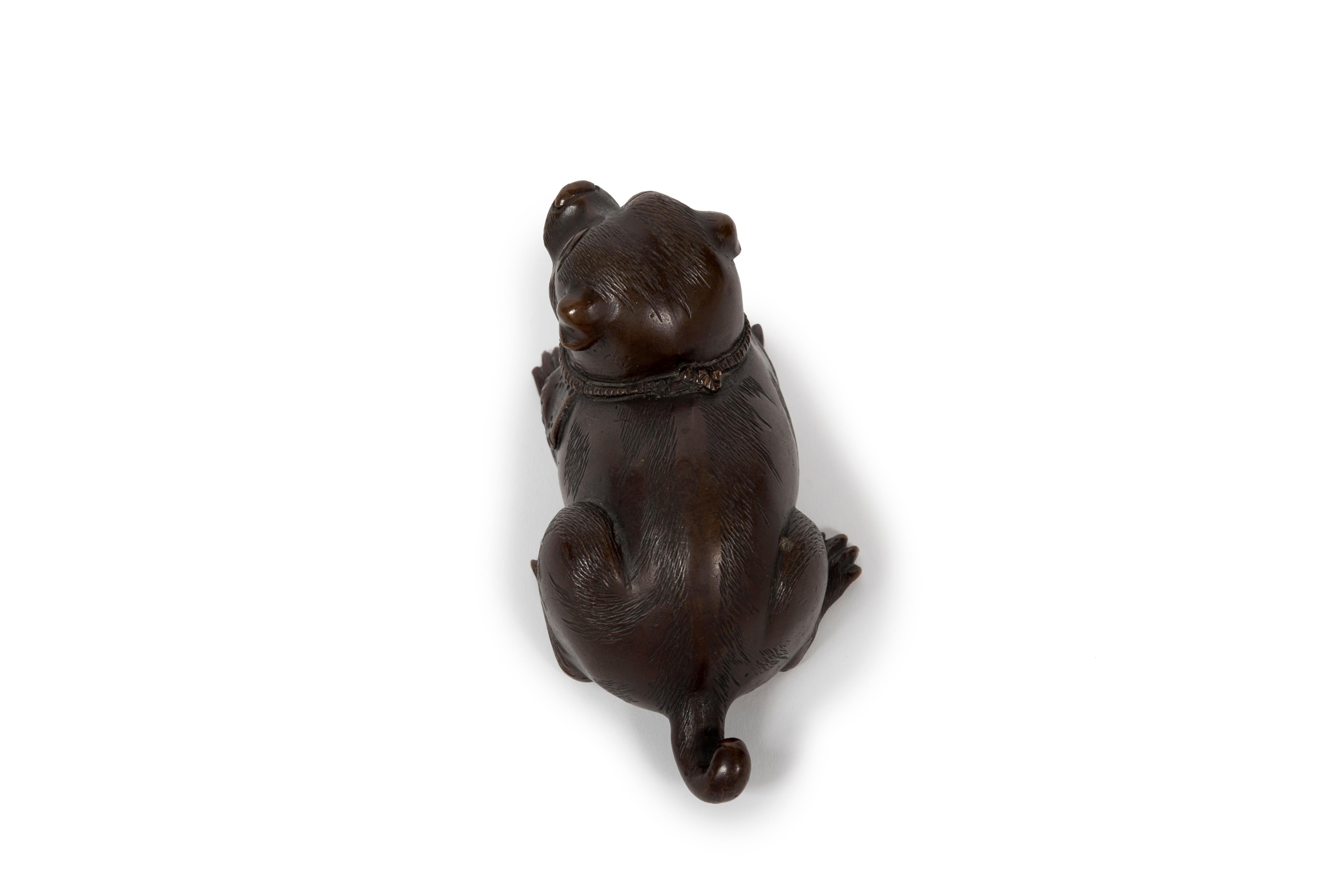 Scultura okimono in bronzo con una patina marrone intenso, che rappresenta un cucciolo sdraiato, probabilmente di razza shiba inu. Questo tipo di soggetto è comune nelle sculture tradizionali di Nippon, questo pezzo specifico ricorda le sculture