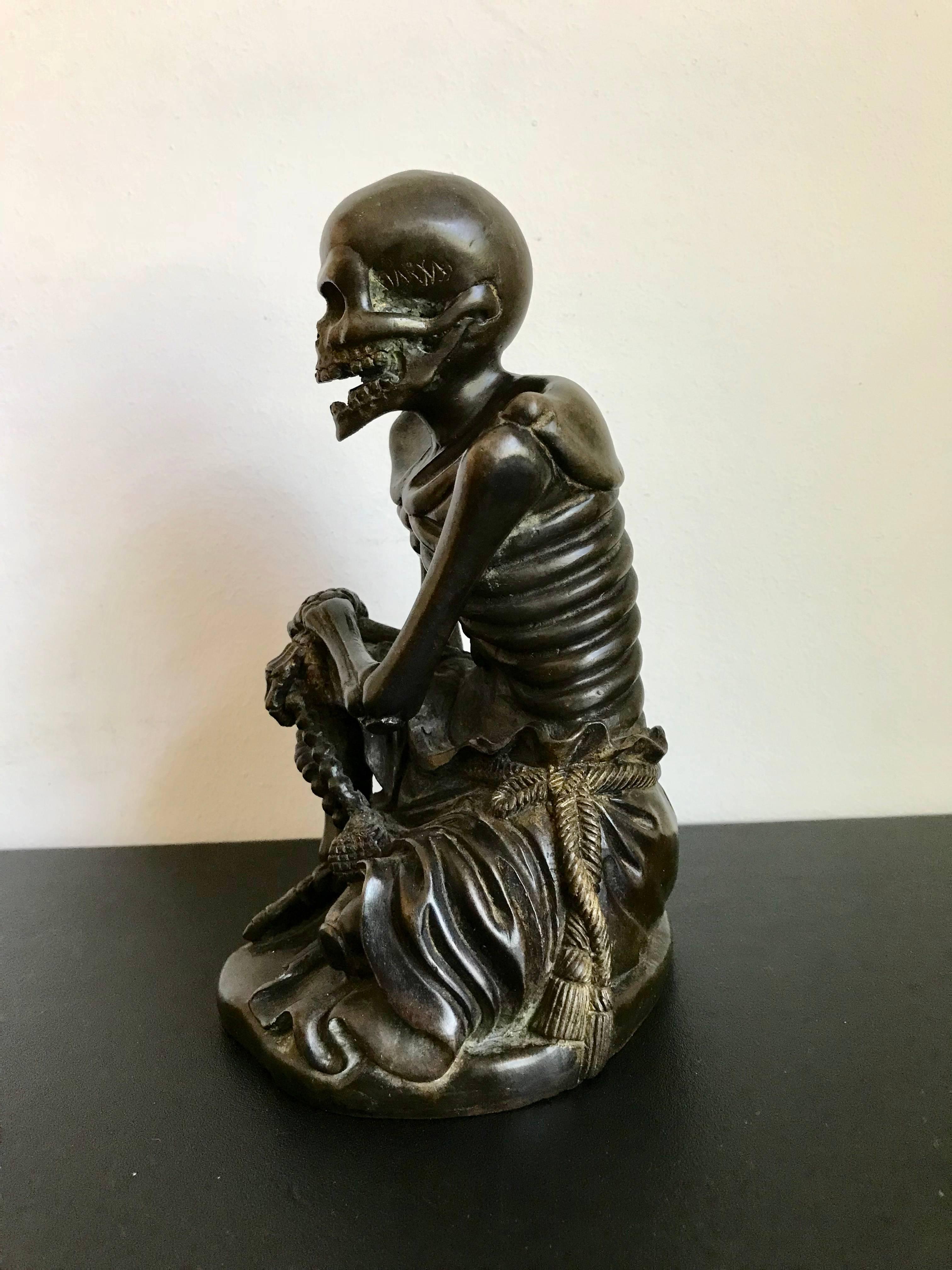 Beautifully cast and intriguing bronze skeleton of a monk shown seated with his robes and rope belt resting around his waist. Traces of gilding to the rope. Possible signature on the skull.