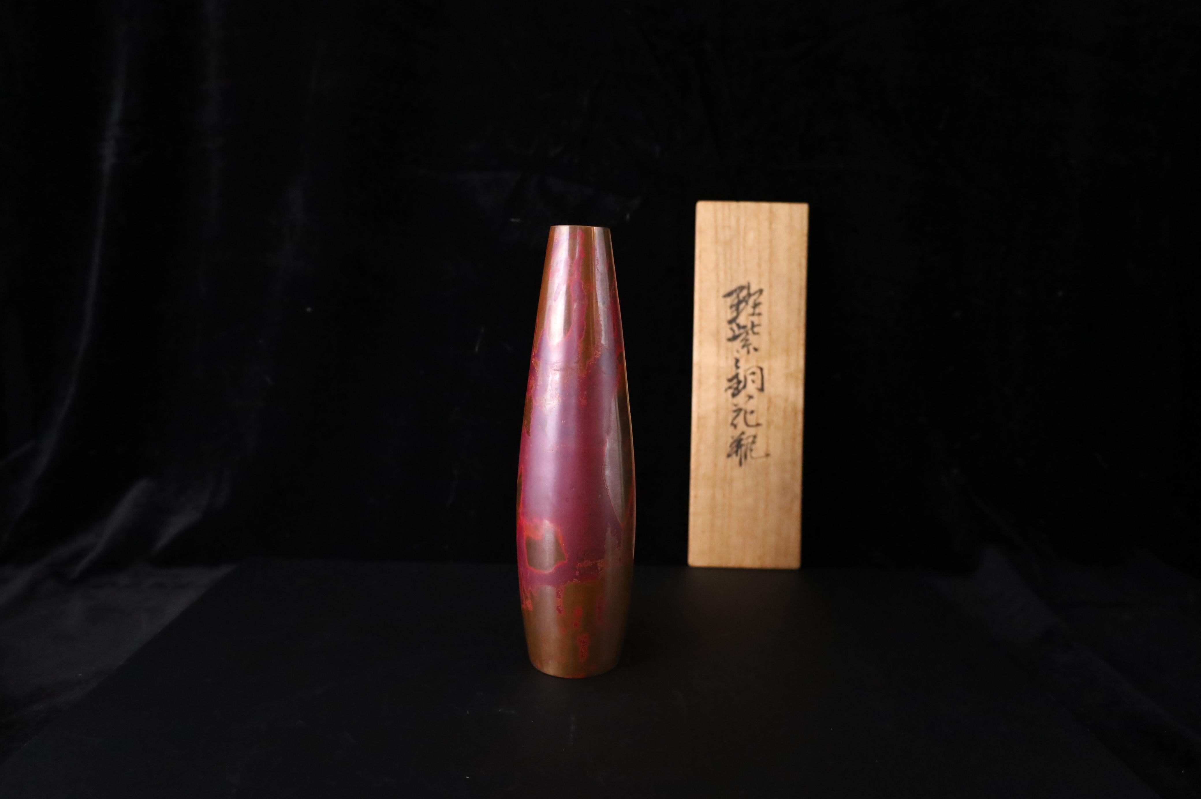 Sorprendente jarrón japonés de bronce martillado a mano, obra del aclamado artista del metal Hara Soemon (四代目晴雲, cuarta generación de Haruseiun), activo durante el periodo Showa.
Elaborado con la técnica Murashido (斑紫銅) -un proceso tradicional de