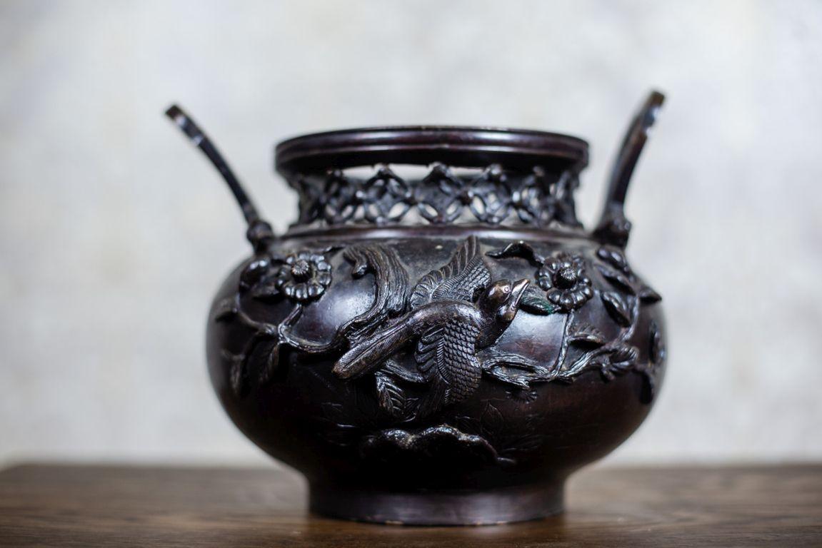 We present you a Japanese vessel from the turn of the 19th and 20th centuries.
The belly is covered with a motif of birds and plants. There is also a handle on each of its side.
Furthermore, the neck is decorated with an openwork ornamental