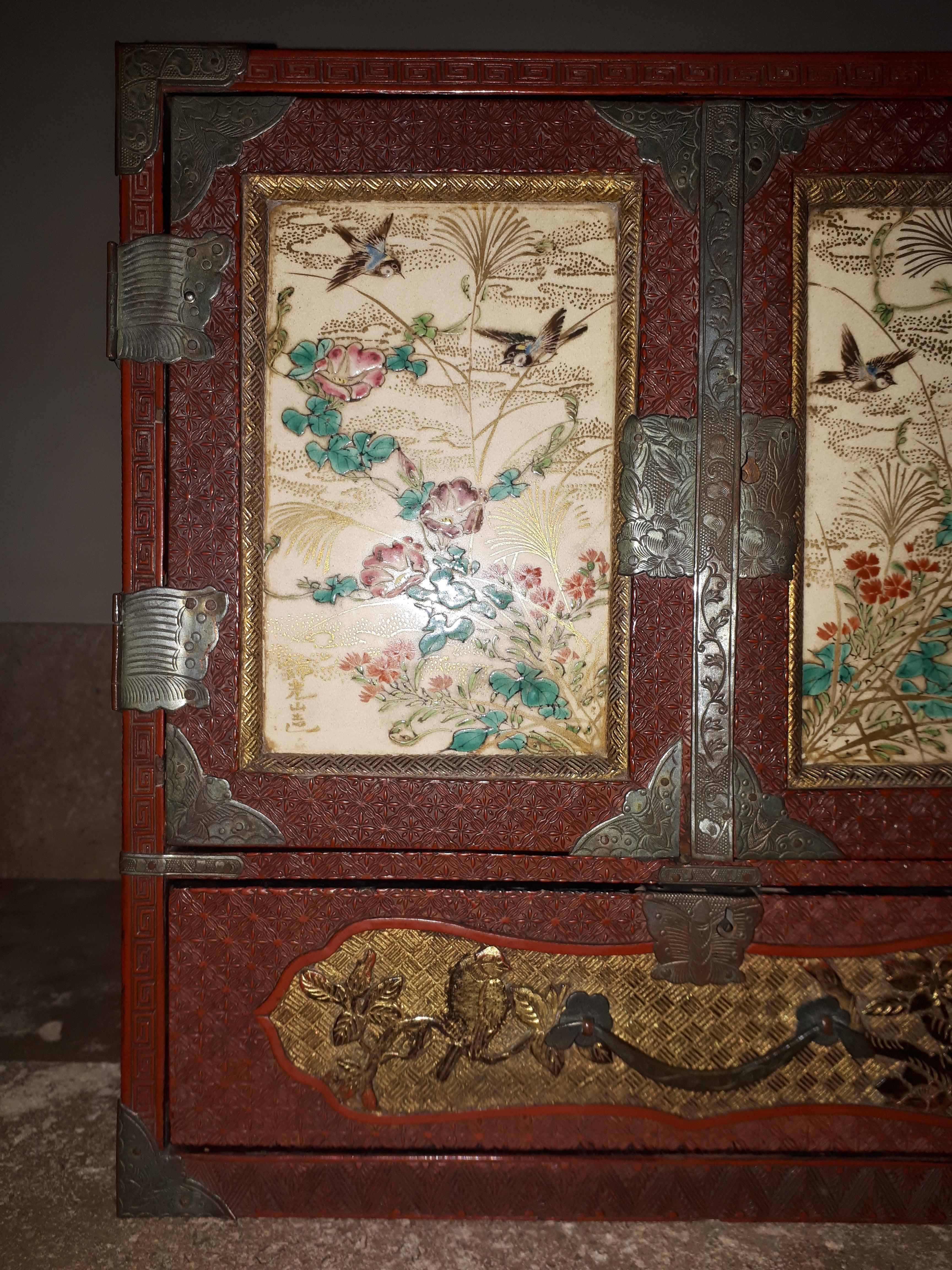 Precious cabinet in carved cinnabar red lacquer with two leaves and a drawer, revealing six small drawers.
The doors are adorned with a porcelain plaque decorated with tits flying among flowers. Each marked with a reputed signature : “Kinkozan zo,”