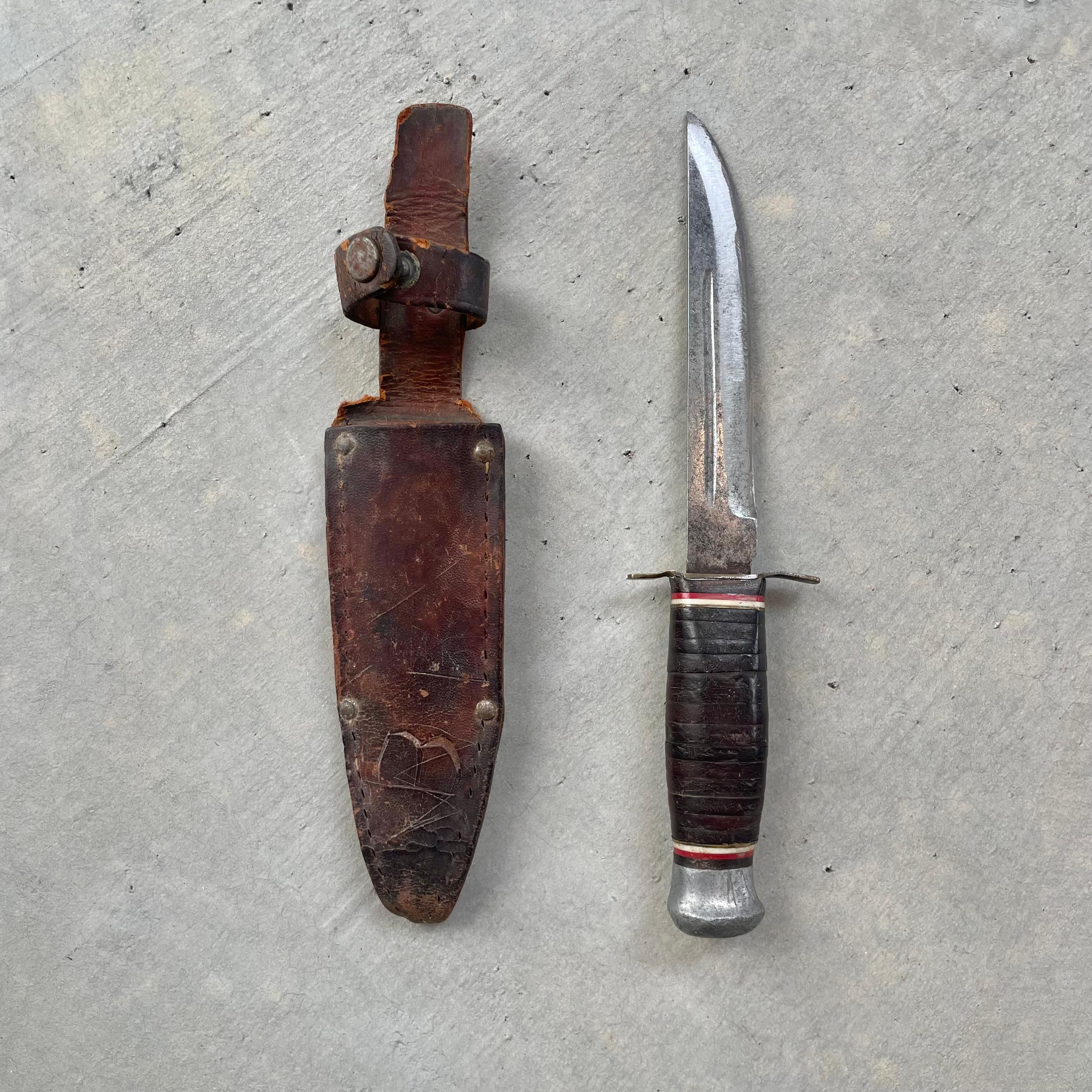 Fantastic Japanese camp knife with a leather sheath. Blade stamped 'Japan.' Traditional stacked leather handle in black with red and white accent rings. Full tang blade running straight through to the pommel. Small metal guard between the blade and