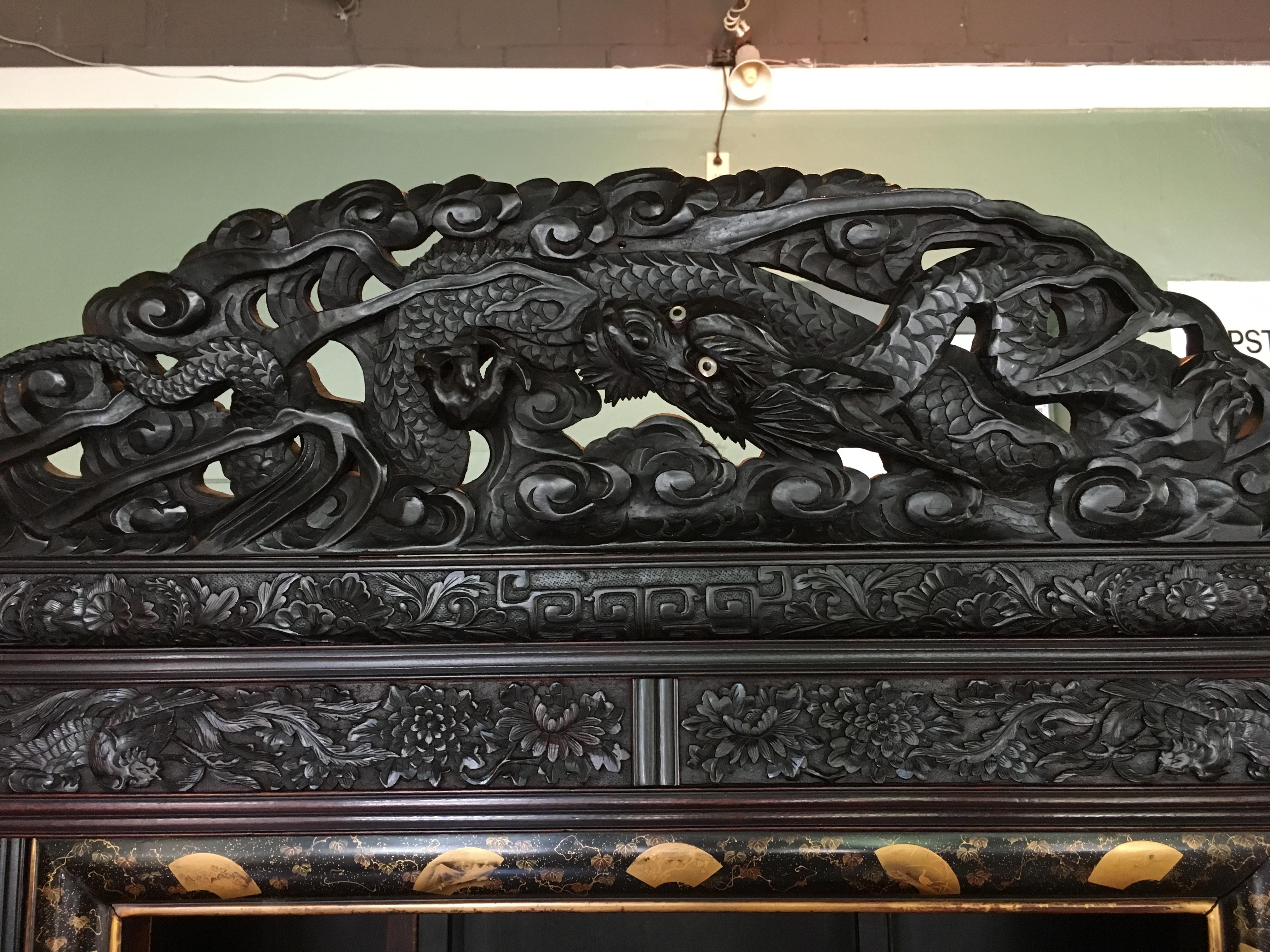 A powerfully carved and ebonized Japanese Meiji Period display cabinet, known as a shodana, made for the Victorian export market.

The cabinet is heavily carved in relief with writhing dragons carved throughout, several featuring mother of pearl