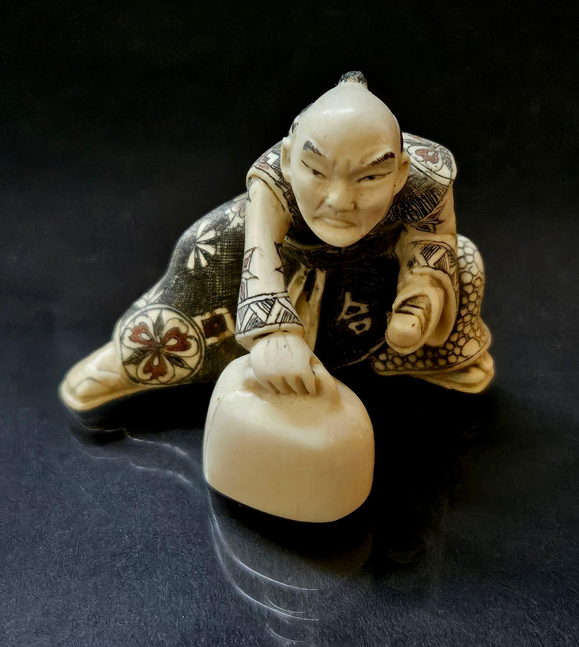 Netsuke Japanese Hand-Carved Polychrome Decorated Figure, Signed on the bottom from the Meiji period. 

A truly hand-carved ivory figure, A man is lifting a weight. It looks like he is challenging himself for his strength, which shows a museum