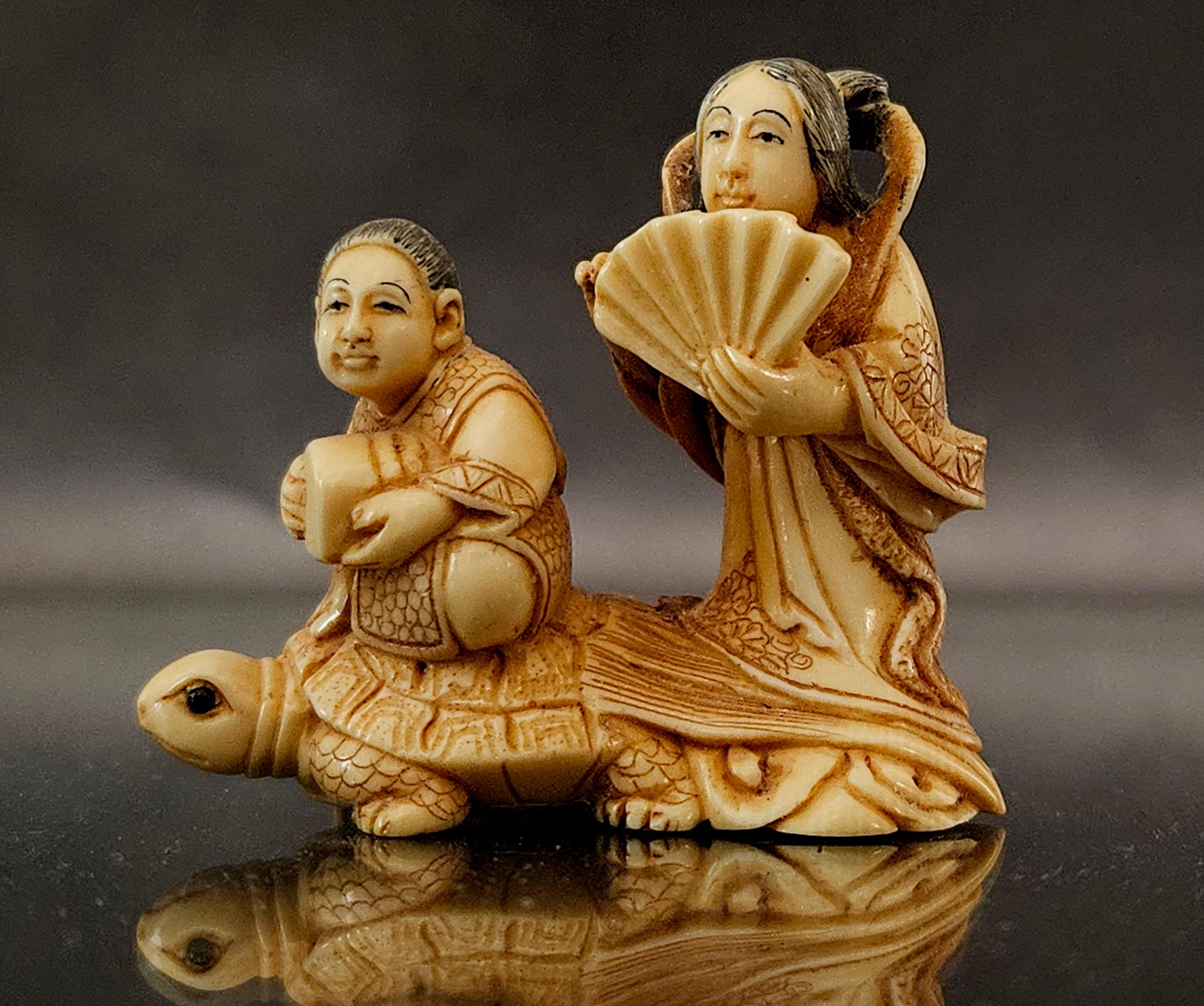 Netsuke Japanese Hand-Carved Polychrome Figure Group depicts a woman standing on a board holding a paper fence, and a boy sitting on the back of a turtle. It looks like the turtle is carrying them on the sea and going to a destination.   Signed on