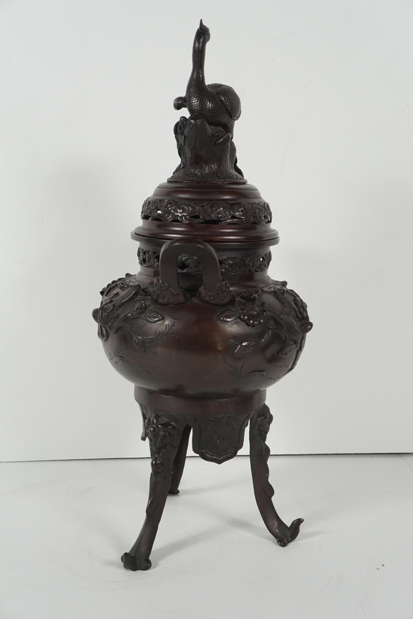 This large scale incense burner was made in the Meiji period in Japanese history. Cast between 1868 and 1900 the censer is topped with a phoenix resting on an open work cloud bordered lid. The body of the censer is cast with foliage, birds and
